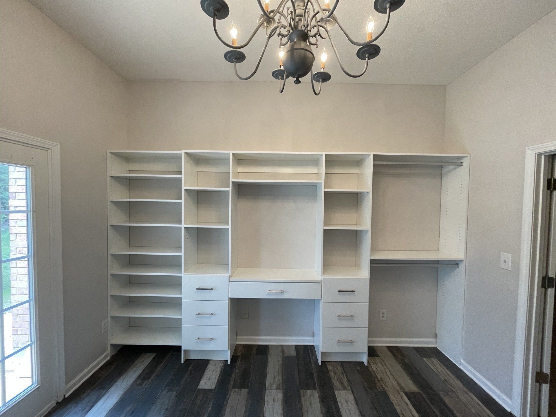 A closet with a desk and shelves and a chandelier hanging from the ceiling.