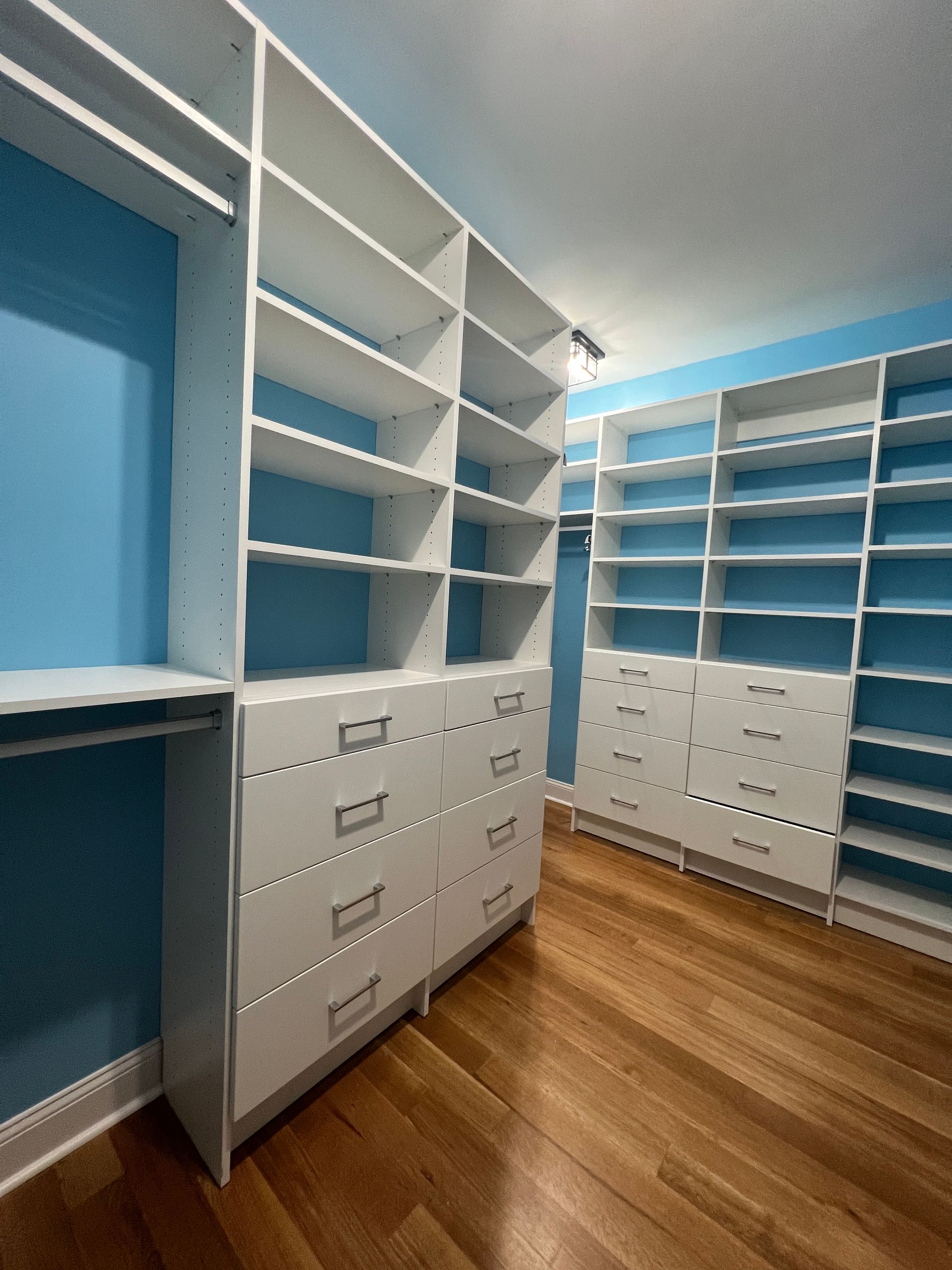 White built-in closet with shelves and drawers against blue walls, wooden floor.