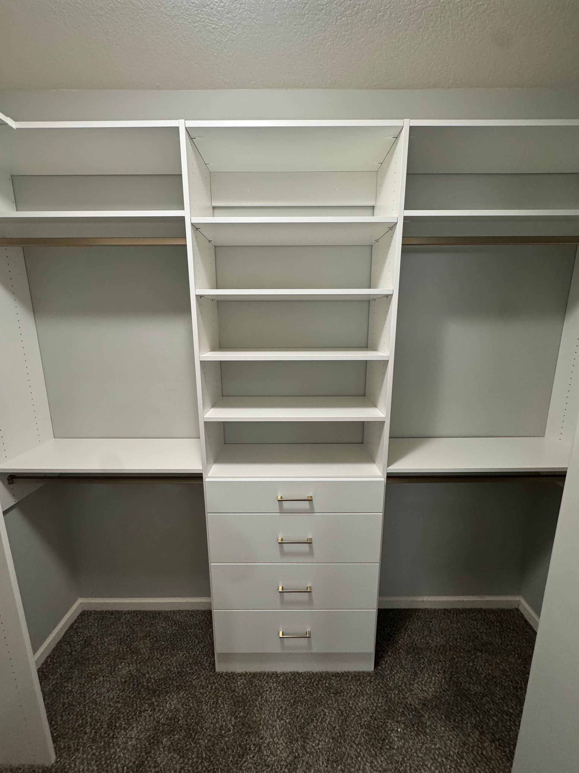 White closet organizer with shelves, drawers, and rods.