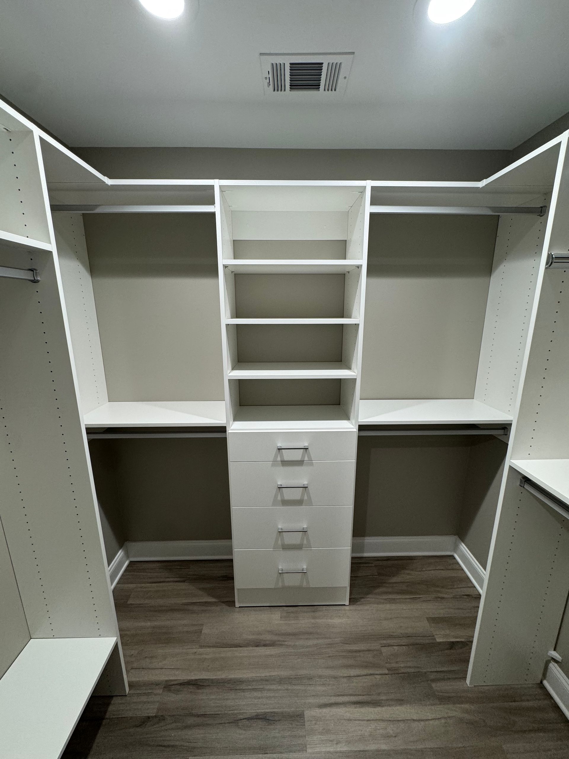 Walk-in closet with white shelving, drawers, and hanging rods.  Grey walls, wood-look flooring.
