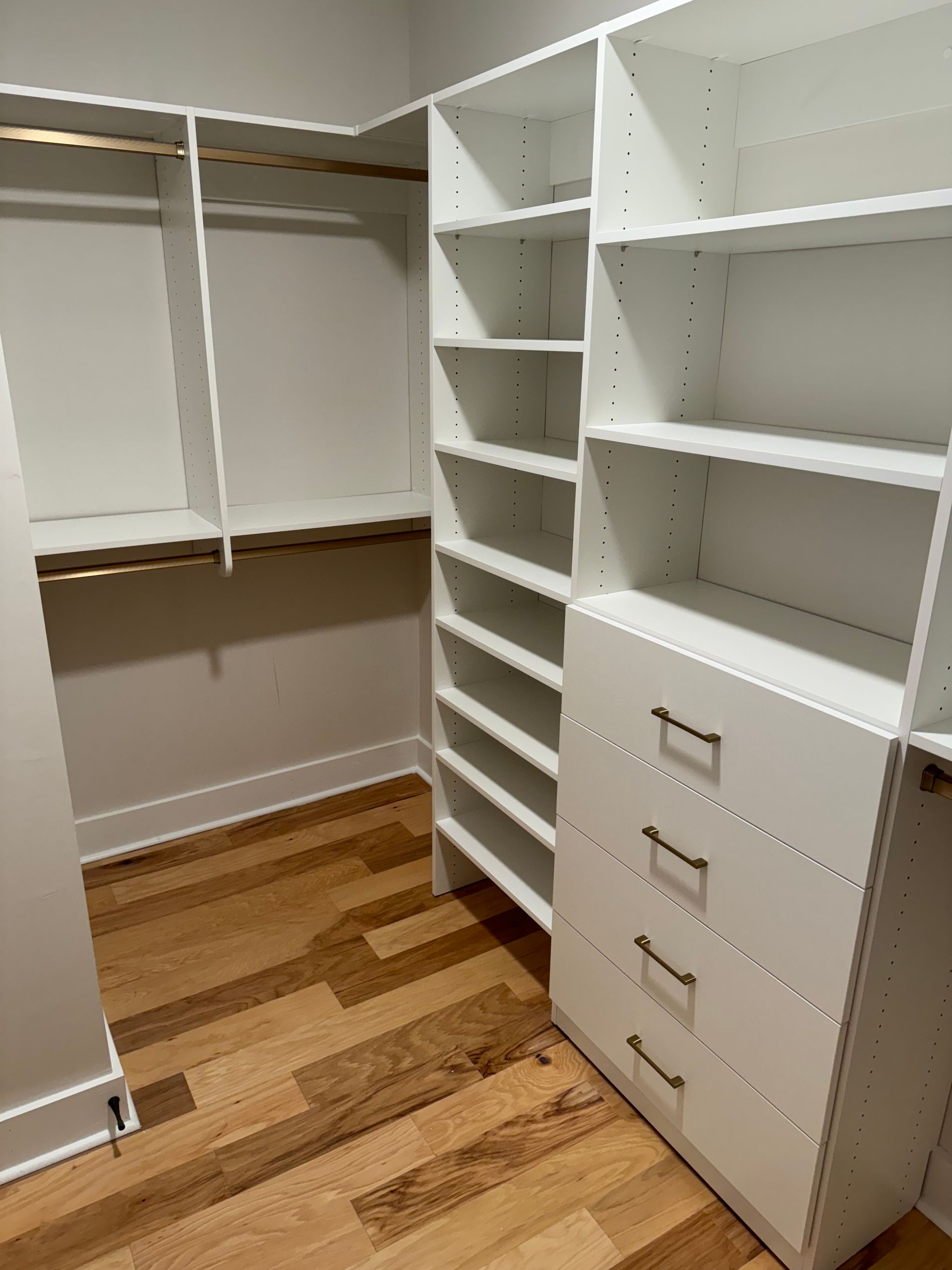 Empty white closet with built-in shelving, drawers, and hanging rods. Hardwood floor.