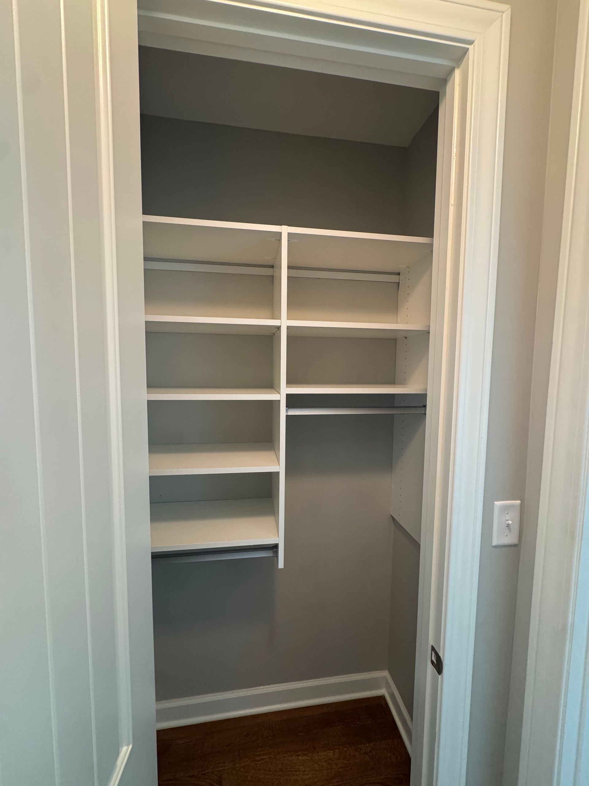 Empty white closet with built-in shelves and a rod, painted gray walls, and a wood floor.