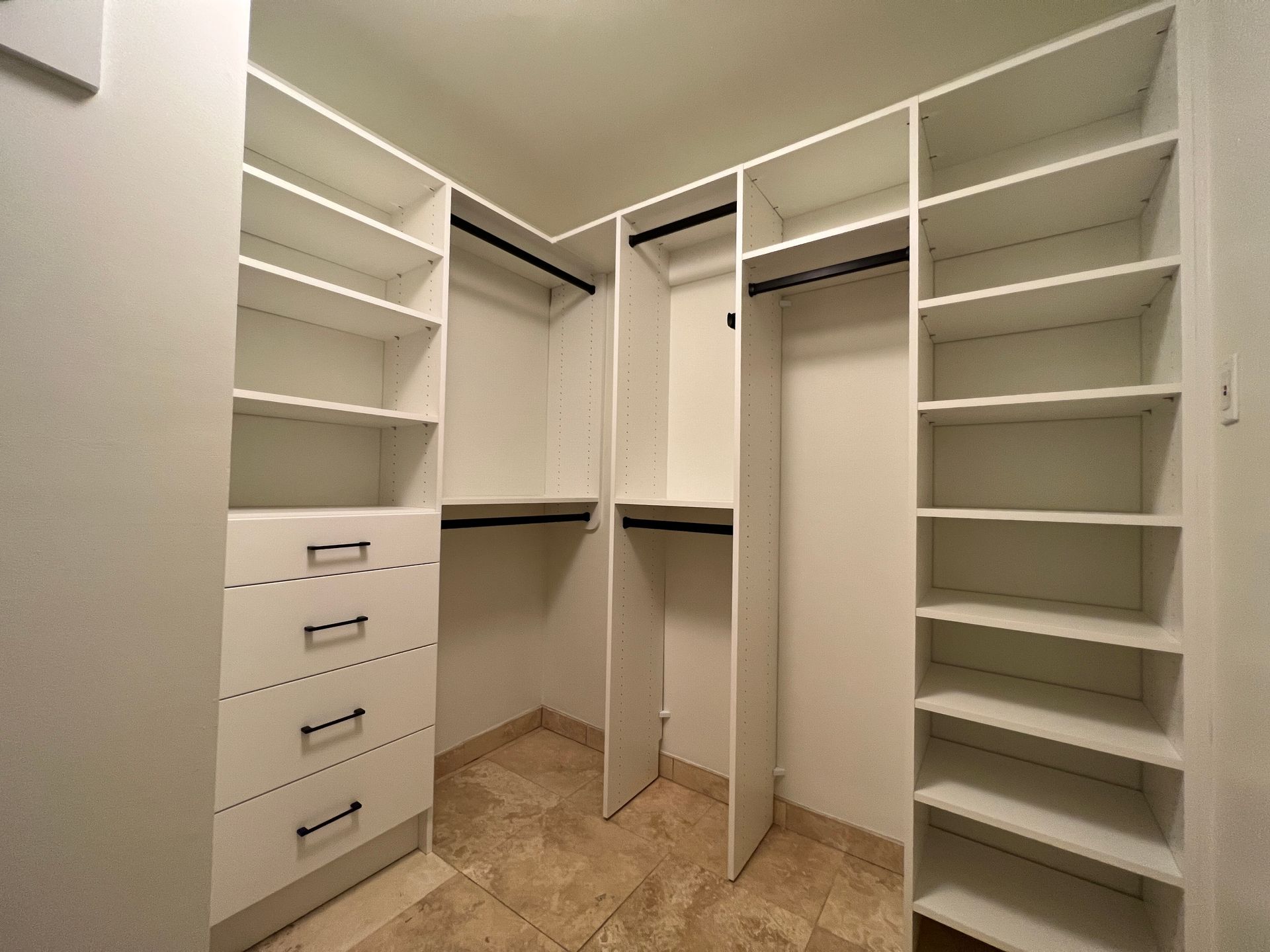 Empty white walk-in closet with shelves, drawers, and hanging rods. Beige tile floor.