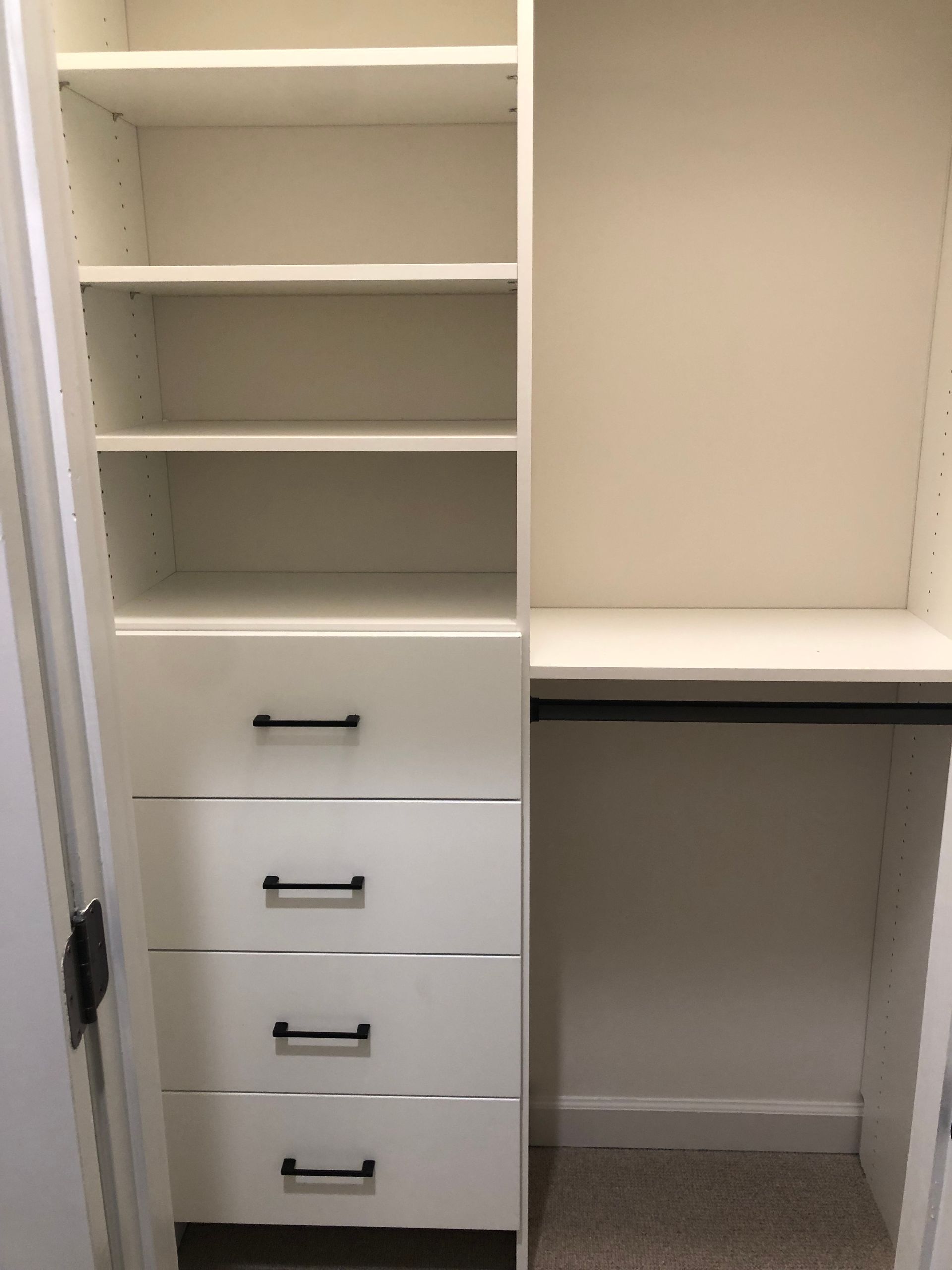 White closet organizer with shelves, drawers, and hanging rod. Black handles.