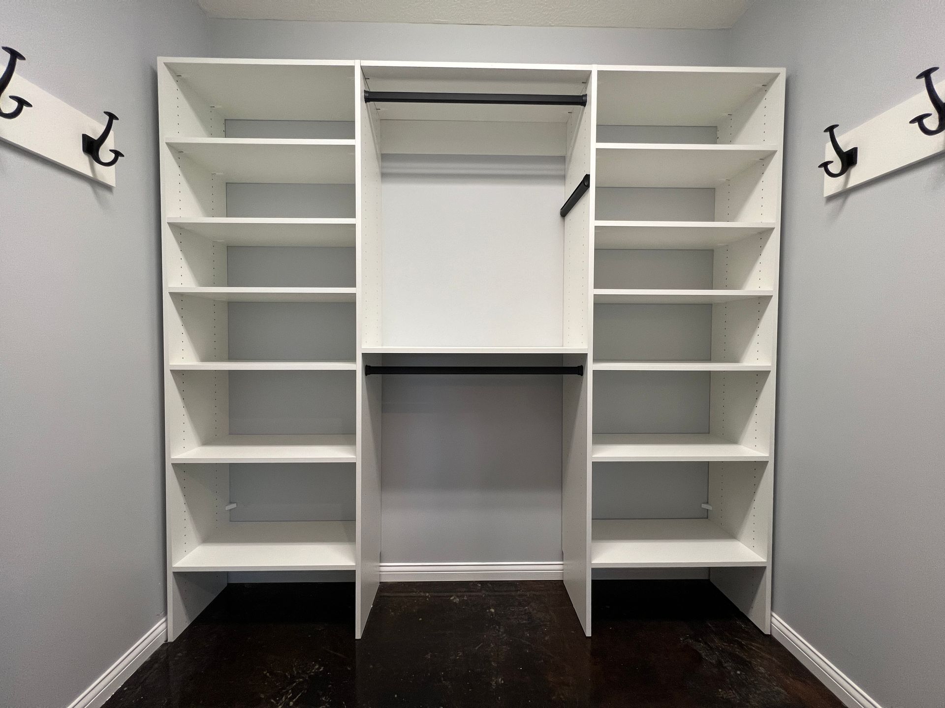 White built-in closet with shelves and hanging rods. Two coat racks on the gray walls.