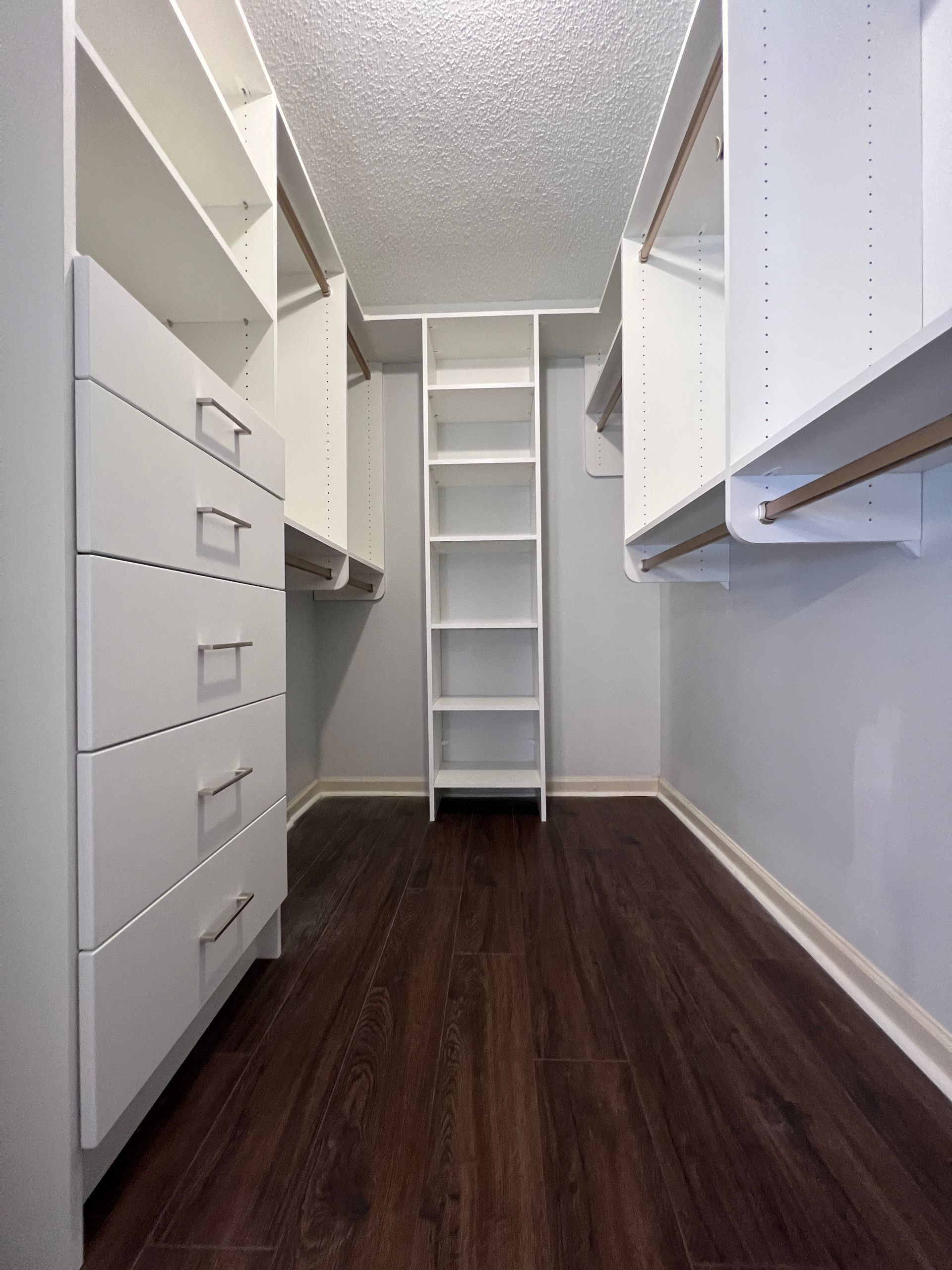 Walk-in closet with white shelves and drawers, dark wood floor, white ladder.
