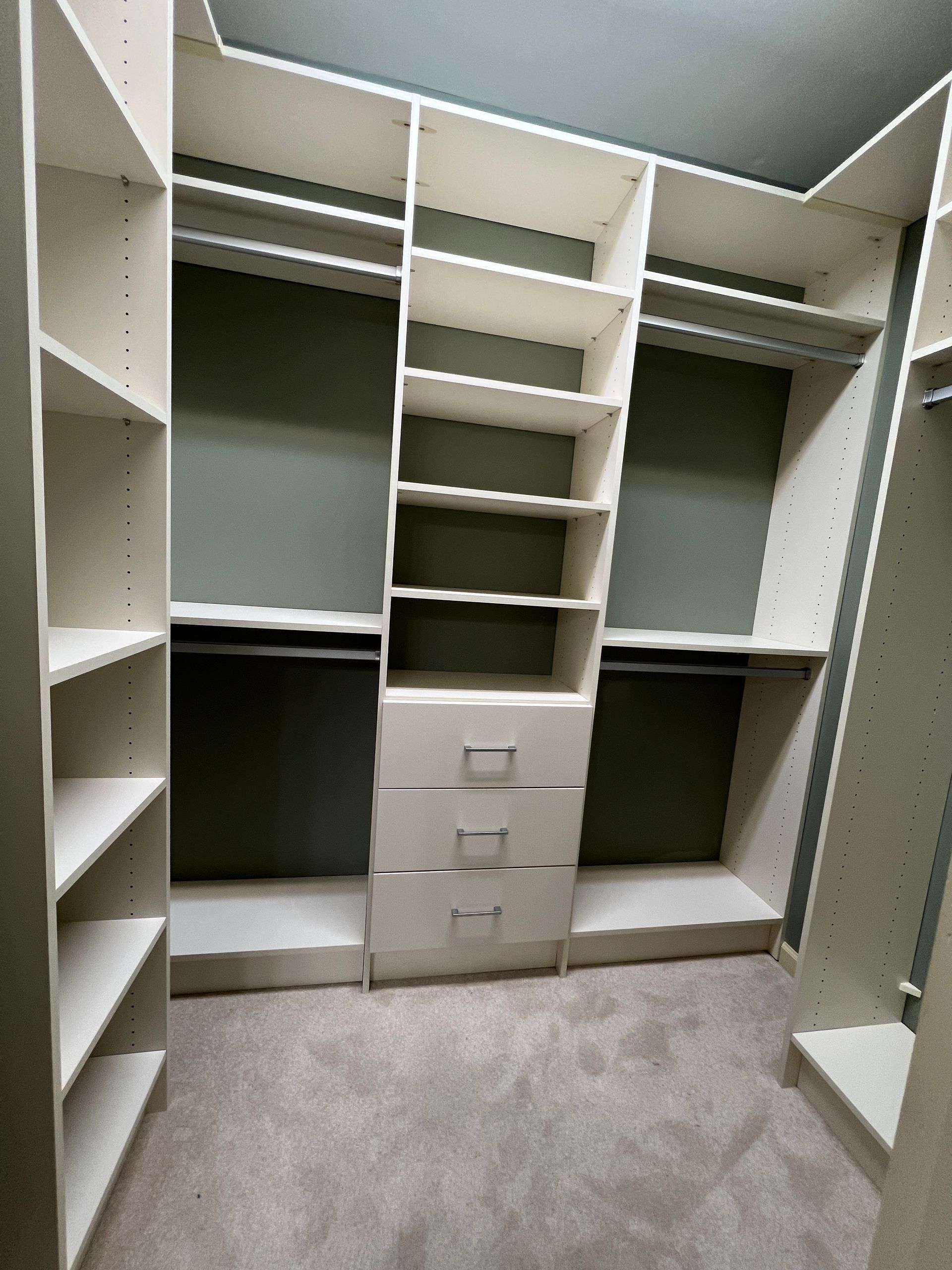 White closet organizer with shelves, hanging rods, and drawers against a gray wall.