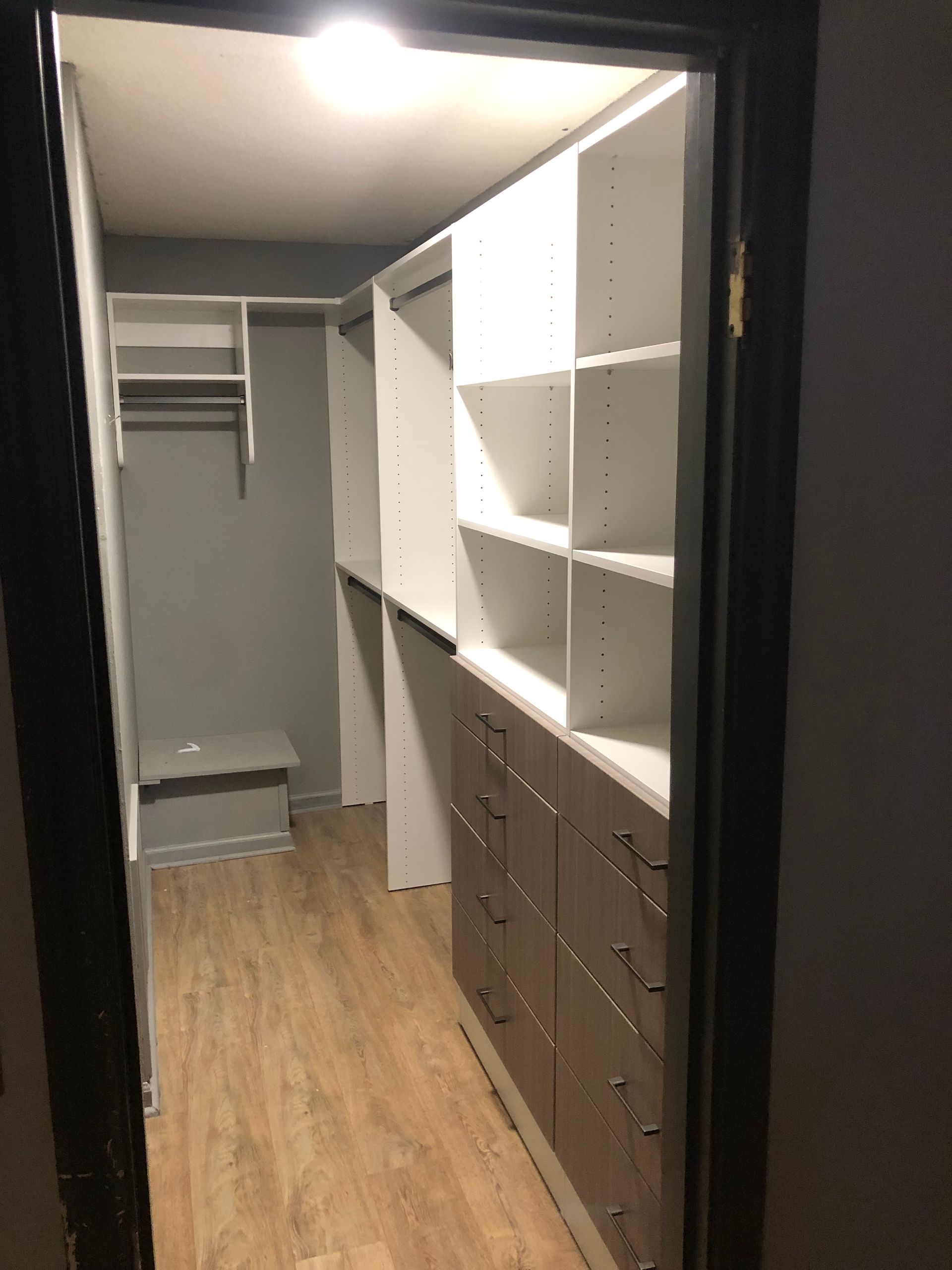 Walk-in closet with white shelves, brown drawers, clothing rod, and a bench. The walls are gray.