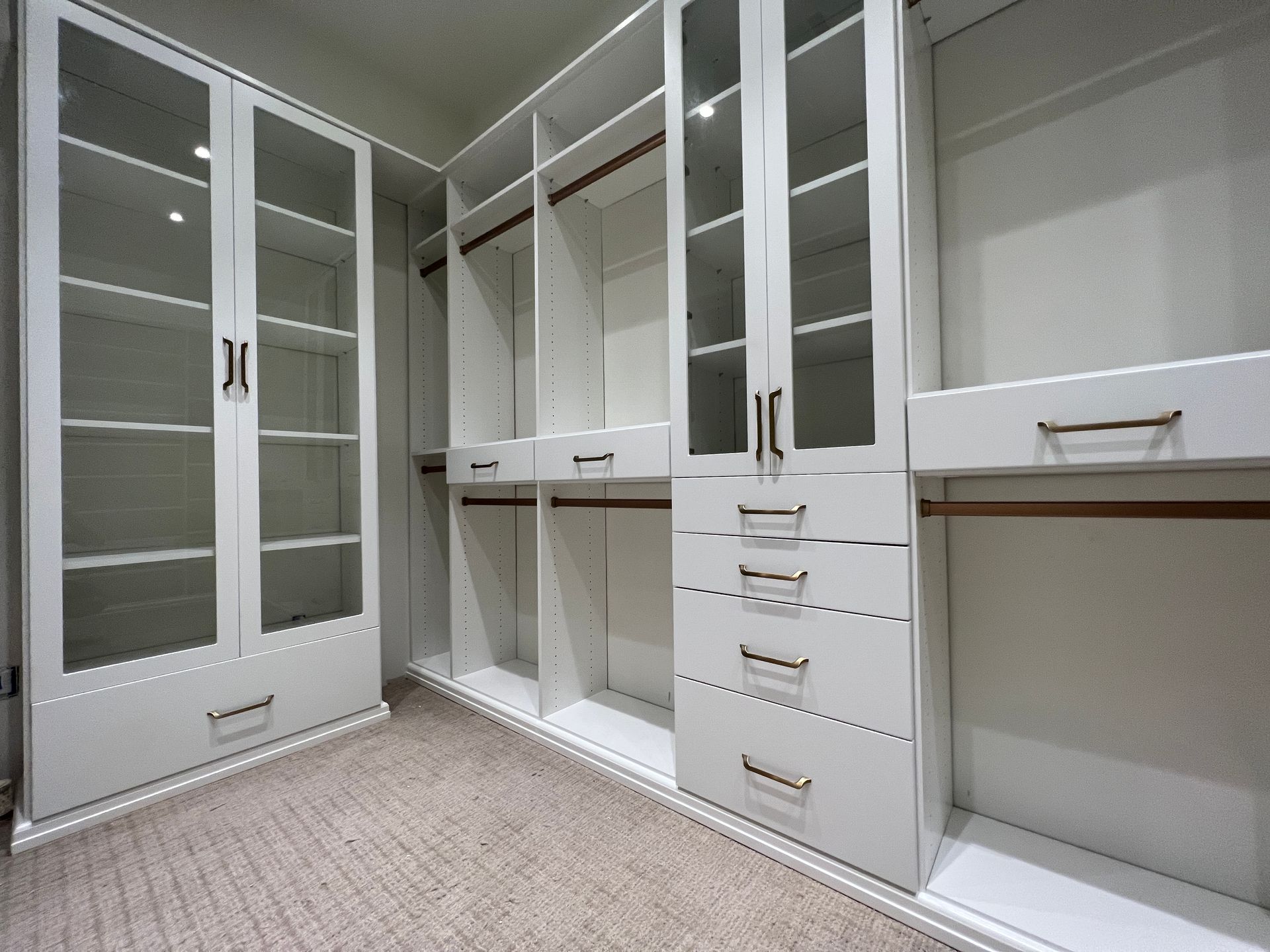 White walk-in closet with glass-door cabinets, drawers, hanging rods, and empty shelves.