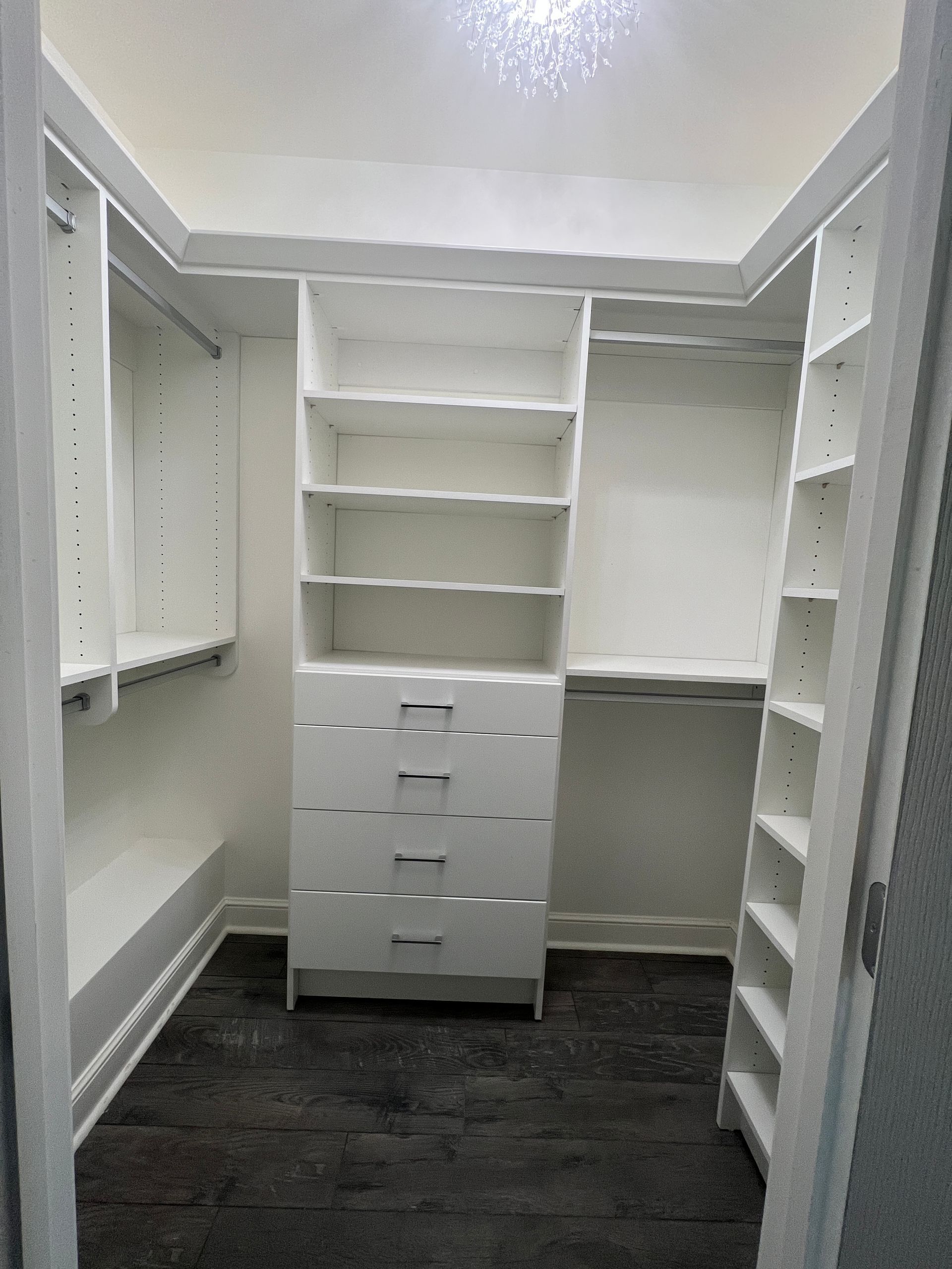 White, organized closet with shelves and drawers. Dark floor, bright overhead lighting.