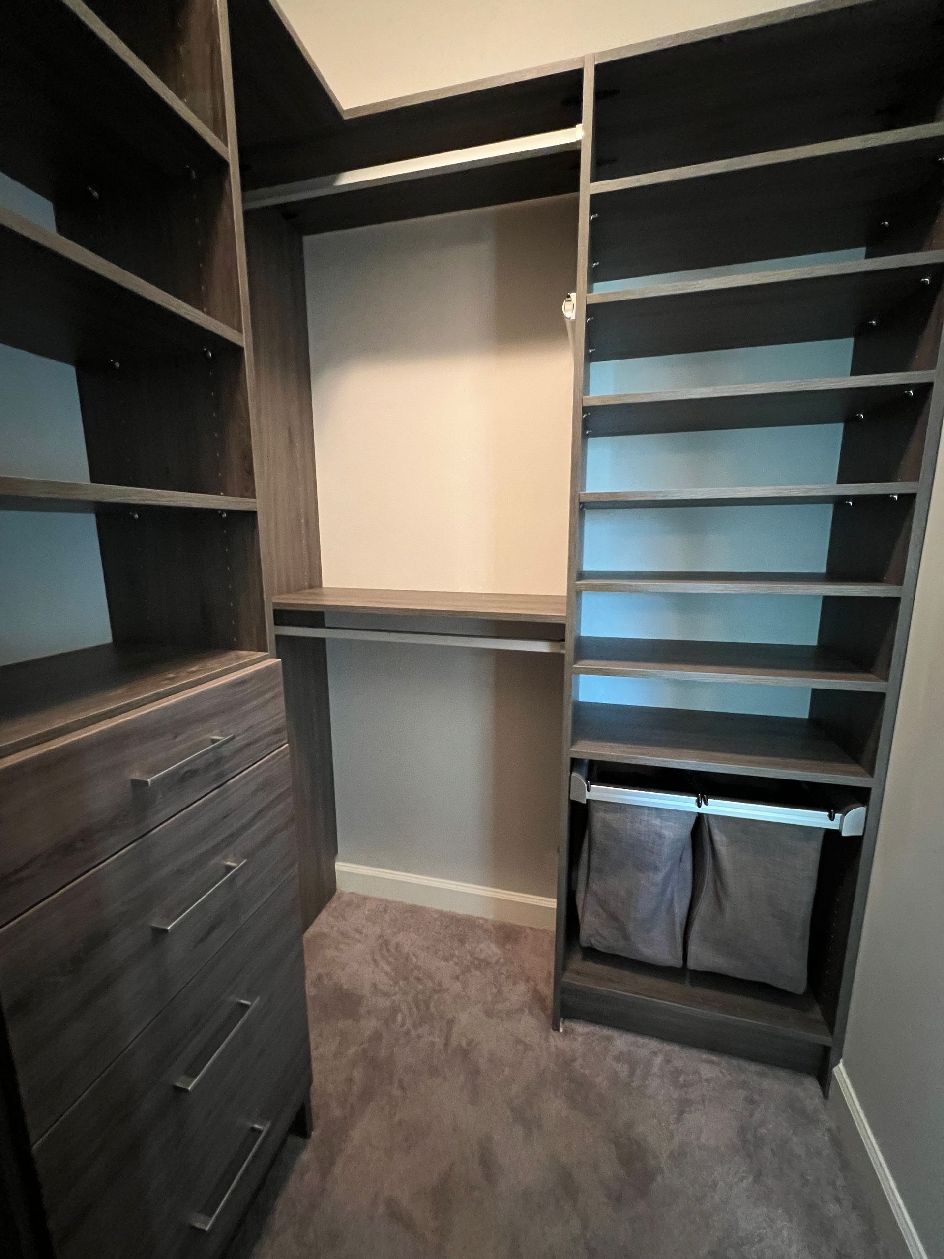 Walk-in closet with dark gray shelving and drawers, carpet, and two cloth storage bins.
