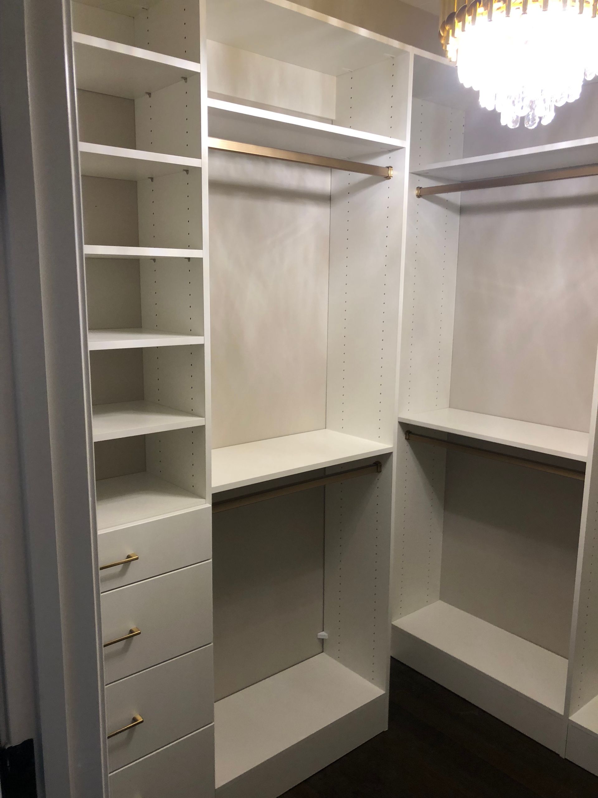 White closet with shelves, drawers, and hanging rods. Golden hardware. Dark wood floor.
