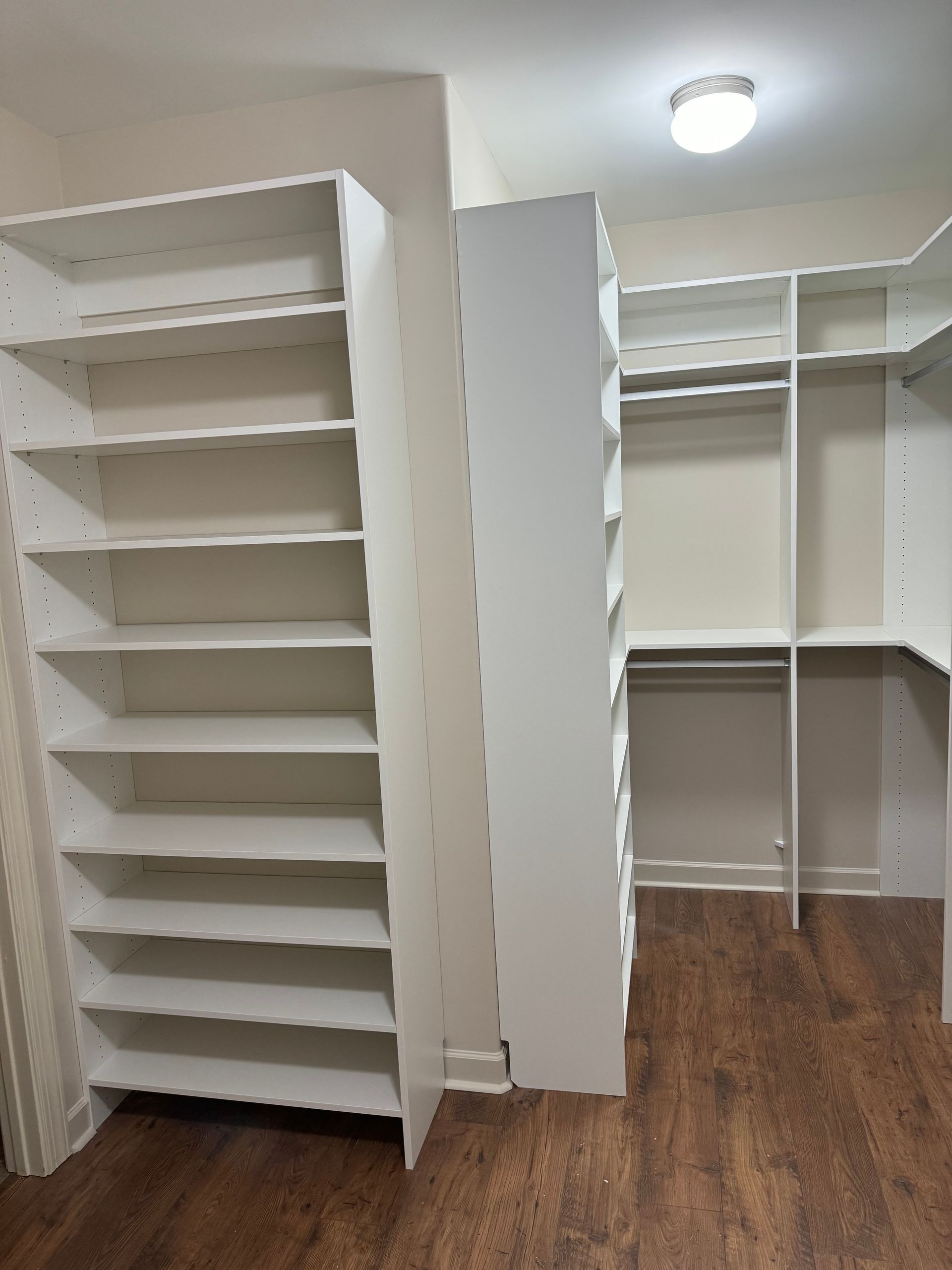 White closet shelving units in a room with hardwood floors and a ceiling light.