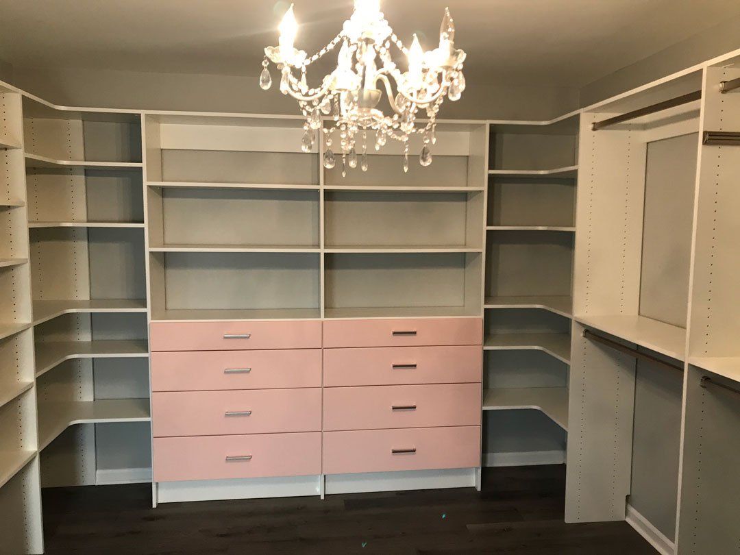 A walk in closet with pink drawers and shelves and a chandelier hanging from the ceiling.