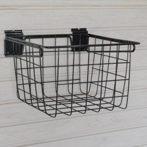 A black wire basket is hanging on a white wall