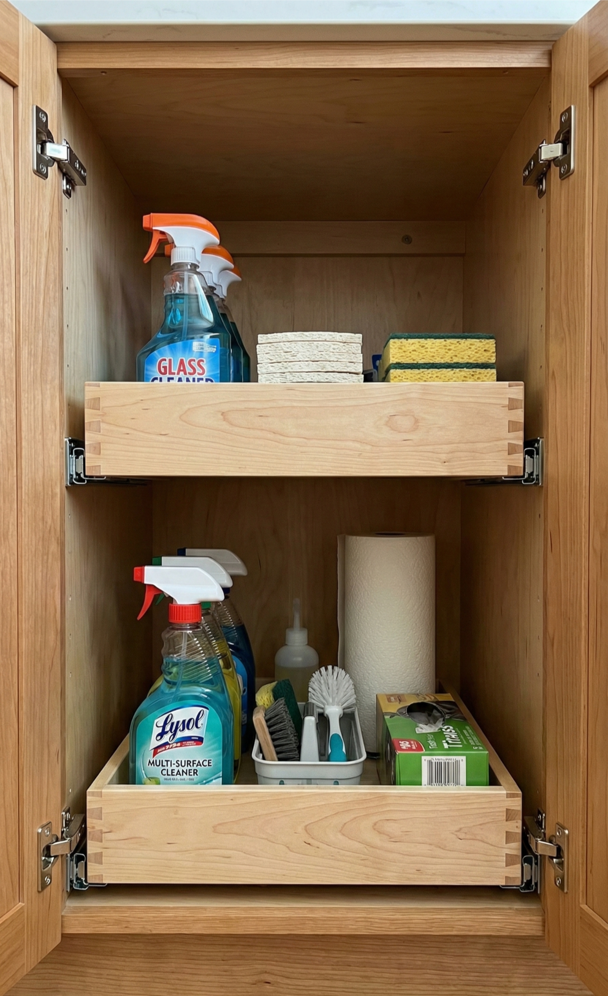 Open cabinet with cleaning supplies on pull-out shelves; spray bottles, sponges, and paper towels.