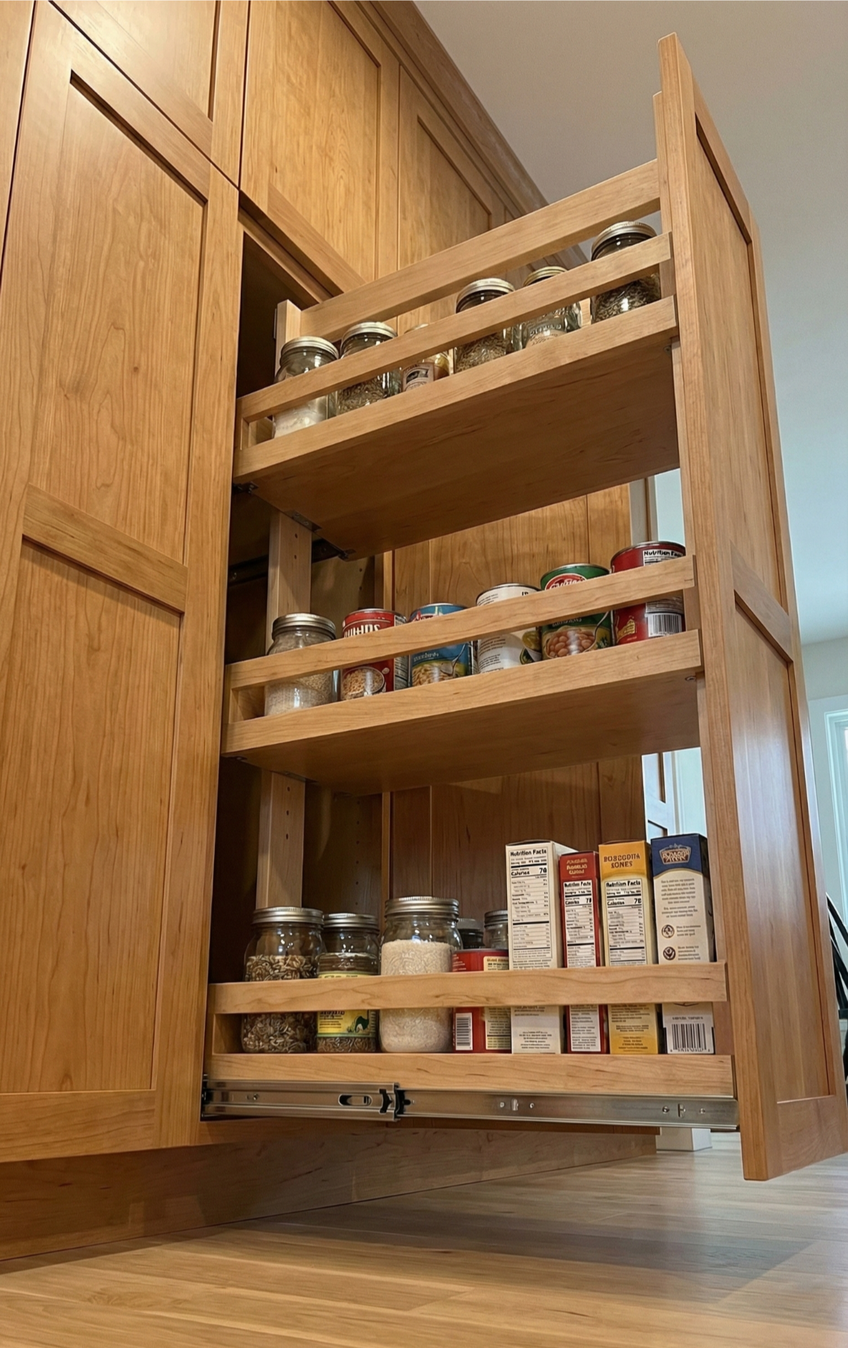 Wooden pull-out kitchen cabinet with various spices and food items on shelves.