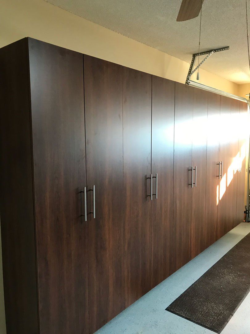 A long row of wooden cabinets in a garage with a ceiling fan.