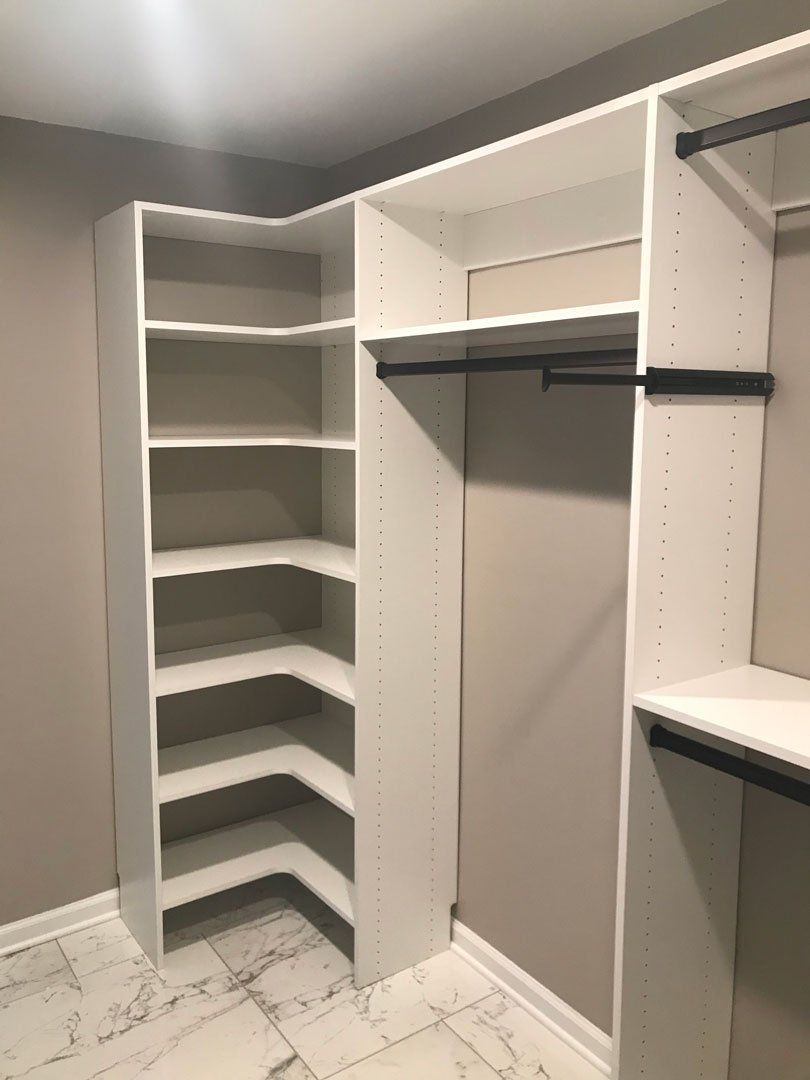 A walk in closet with white shelves and a marble floor.