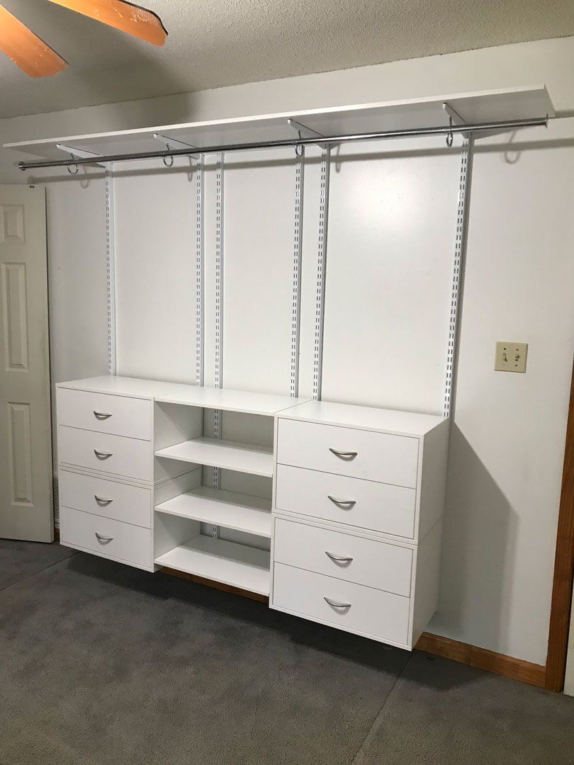 A closet with white shelves and drawers and a ceiling fan