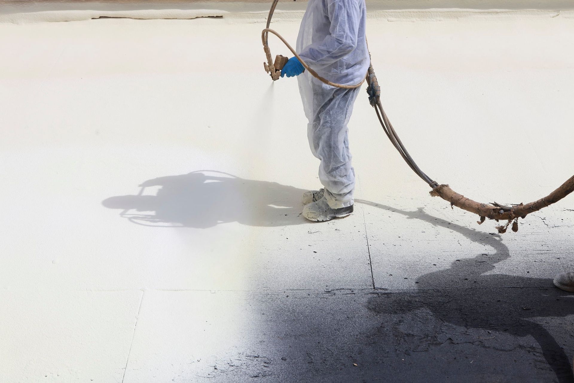 A man is spraying a white and black coating on a roof.