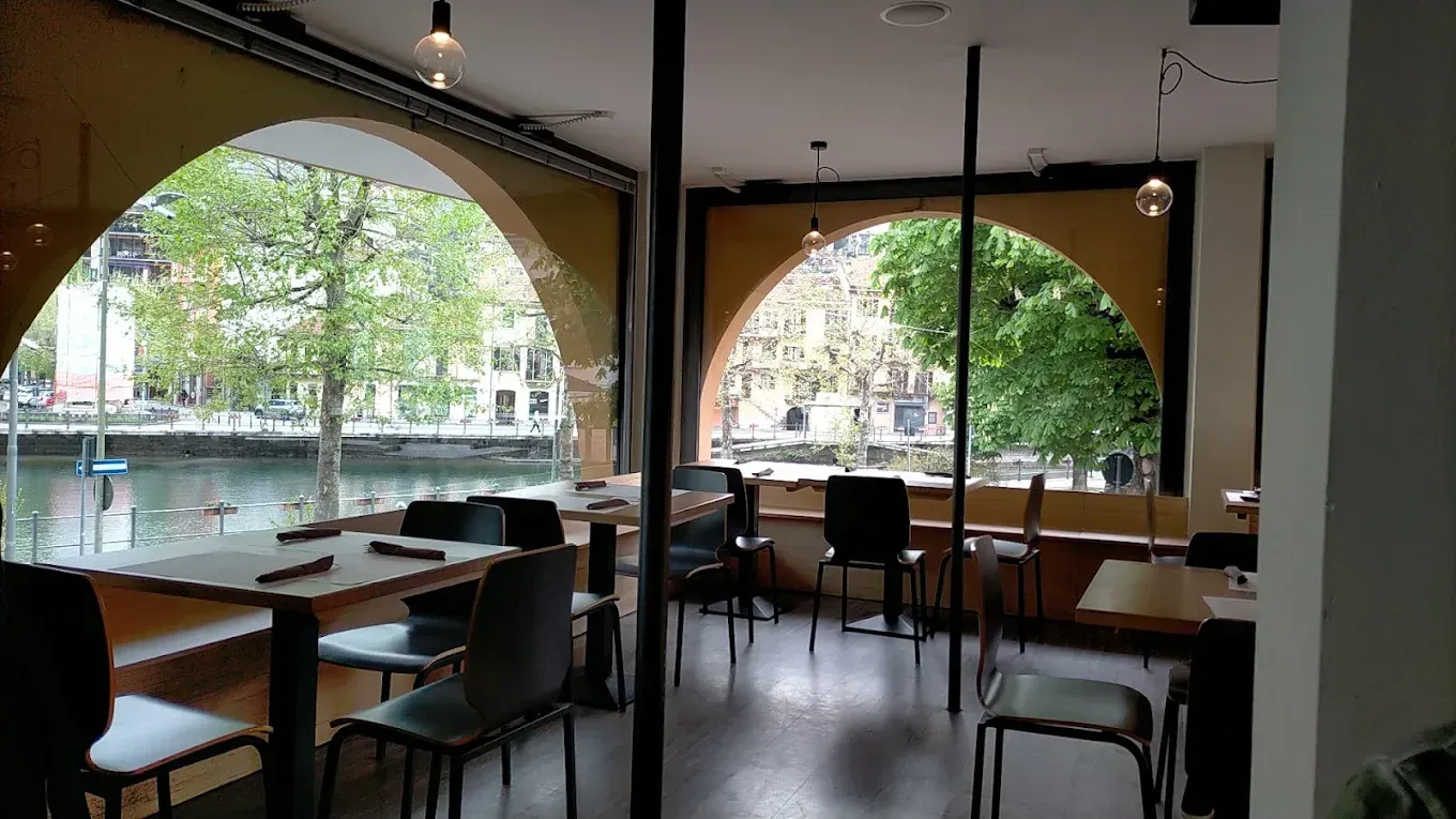 Un piatto di spaghetti con pomodorini, erbe aromatiche e capperi, con olio d'oliva e una ciotola da portata sullo sfondo.