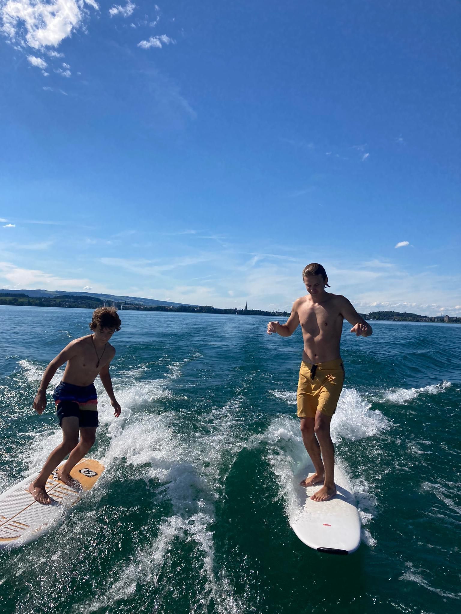 Two men are riding a wave on a surfboard on the lake 