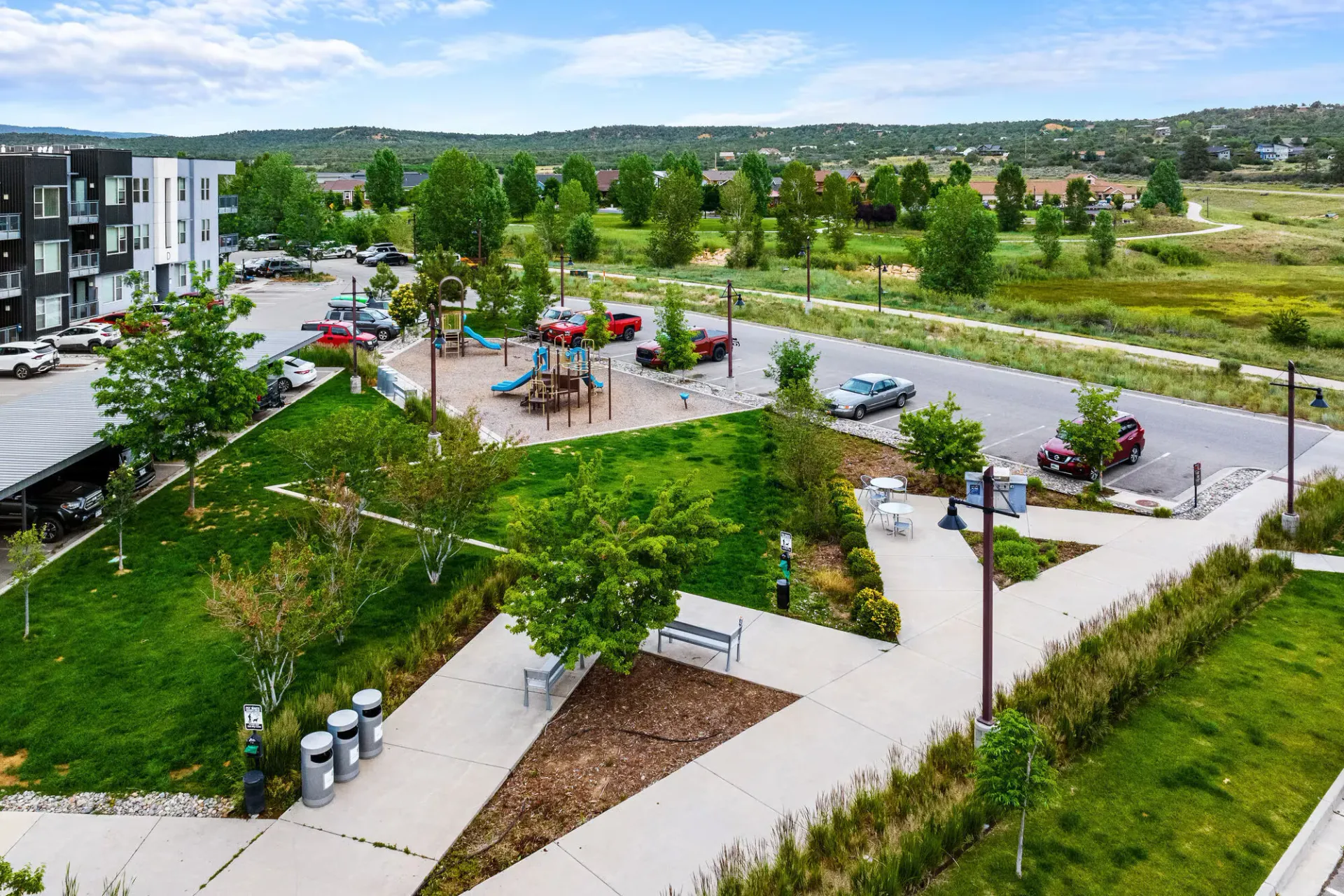 Aerial view of apartment community with a playground, trees, and parking.