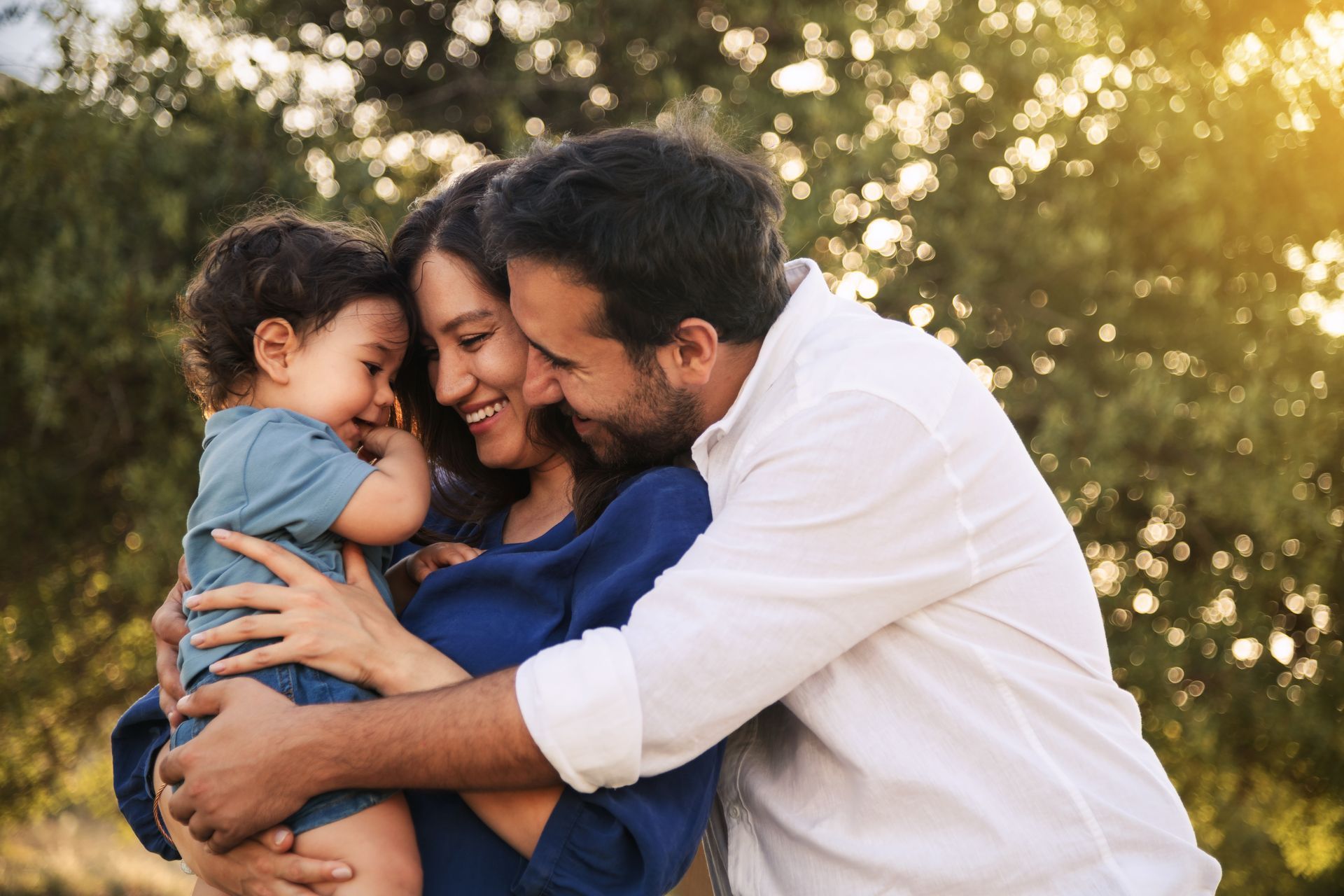 Family embracing outdoors, smiling. Woman and man hug toddler at Tradewinds Apartments