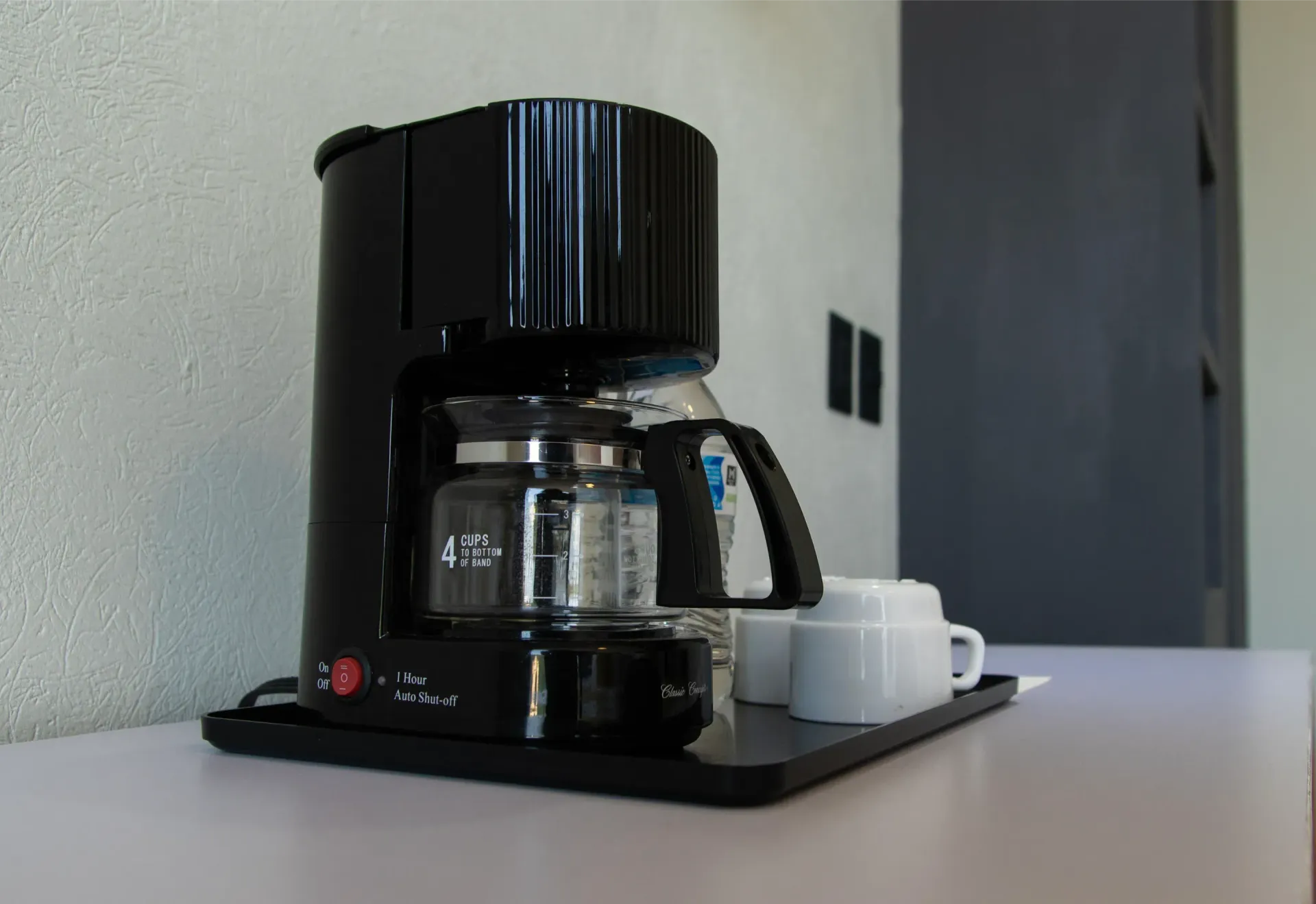 Cafetera negra sobre la encimera de la cocina con una taza blanca al lado.