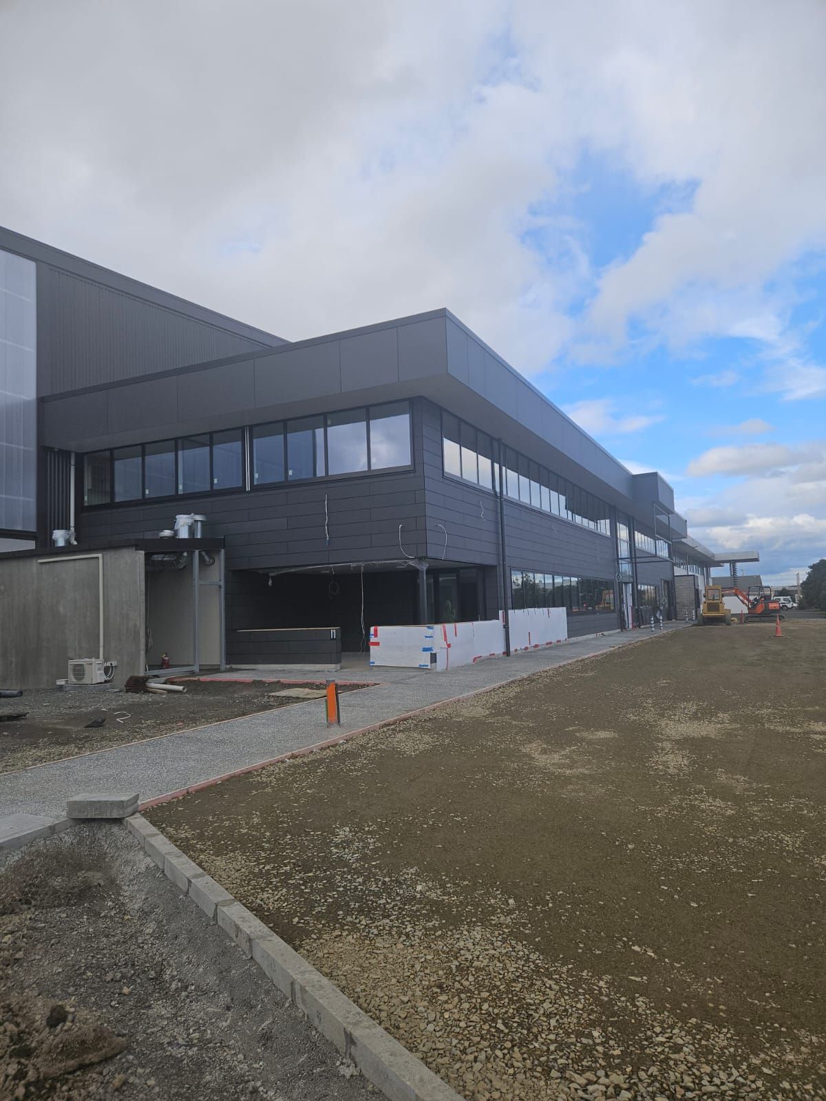 Modern two-story building under construction with dark grey facade and large windows; cloudy sky.