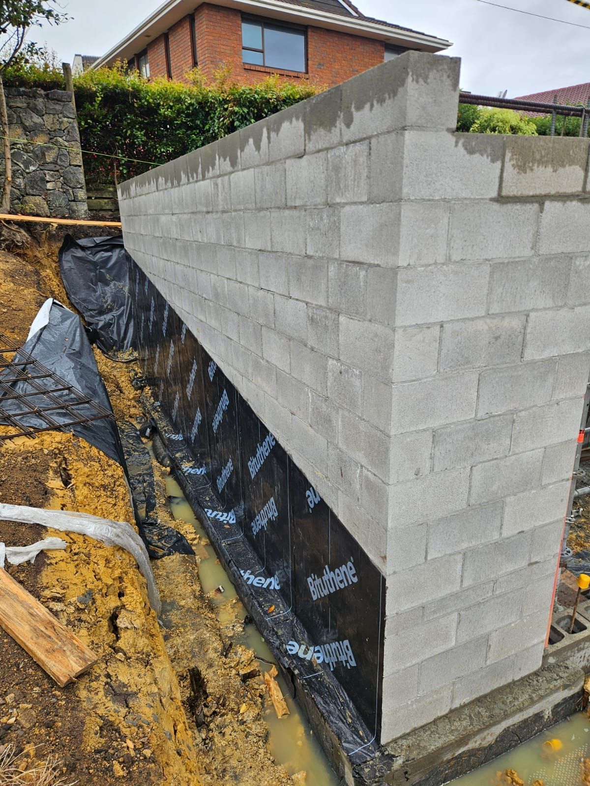 Block wall construction. Concrete blocks, black waterproof membrane, muddy trench.
