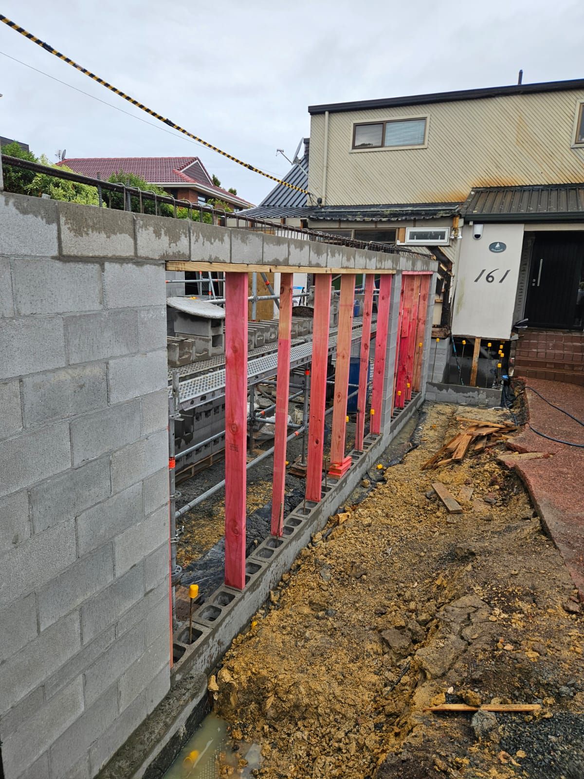 Construction site: cinder block wall with red supports, alongside a driveway.