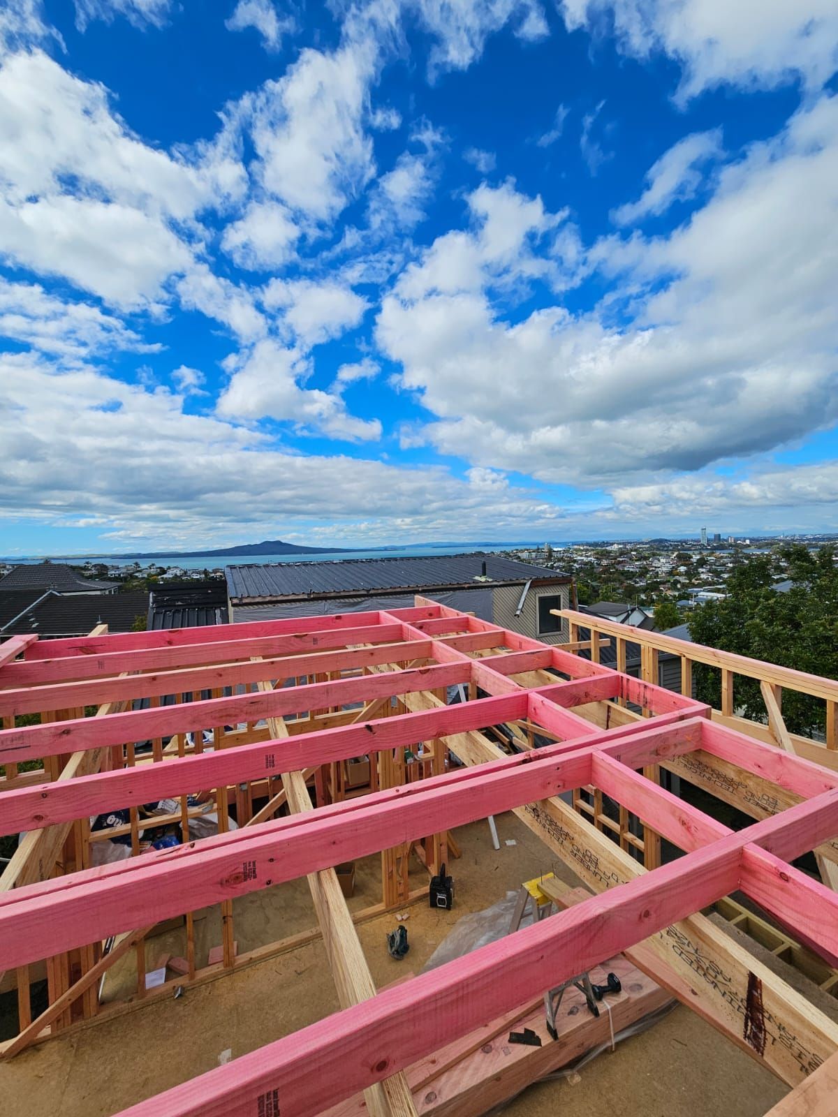 Roof framing of a house under construction with a blue sky and distant city view.