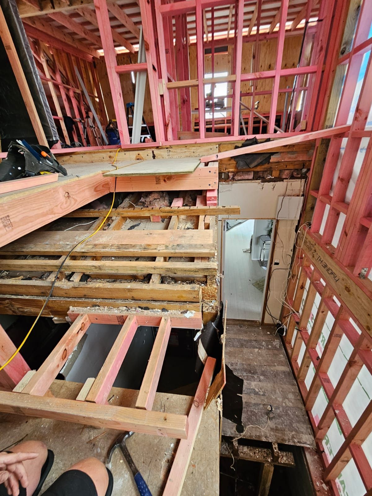 Construction site: exposed wood framing of a room and staircase. Pink studs, open floor, and ceiling.