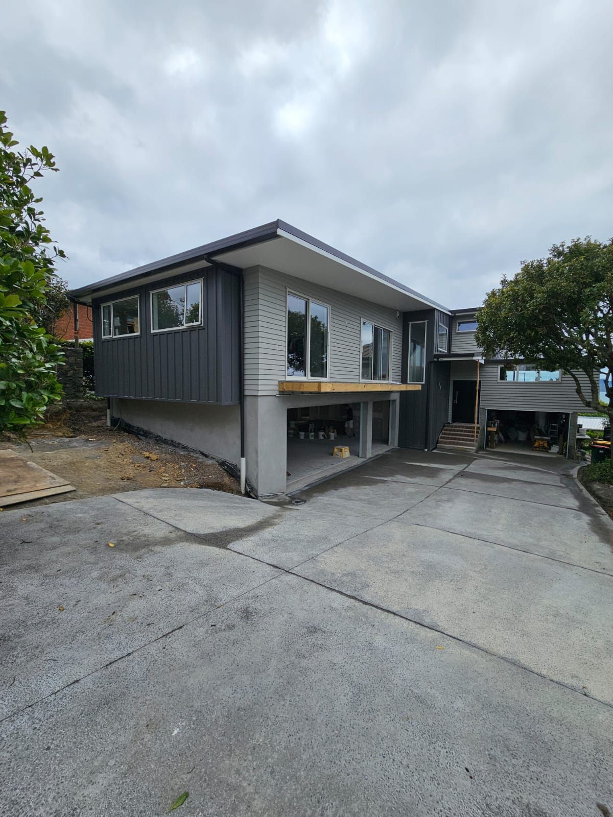 Modern two-story house with gray and dark siding. Concrete driveway in front. Overcast sky.