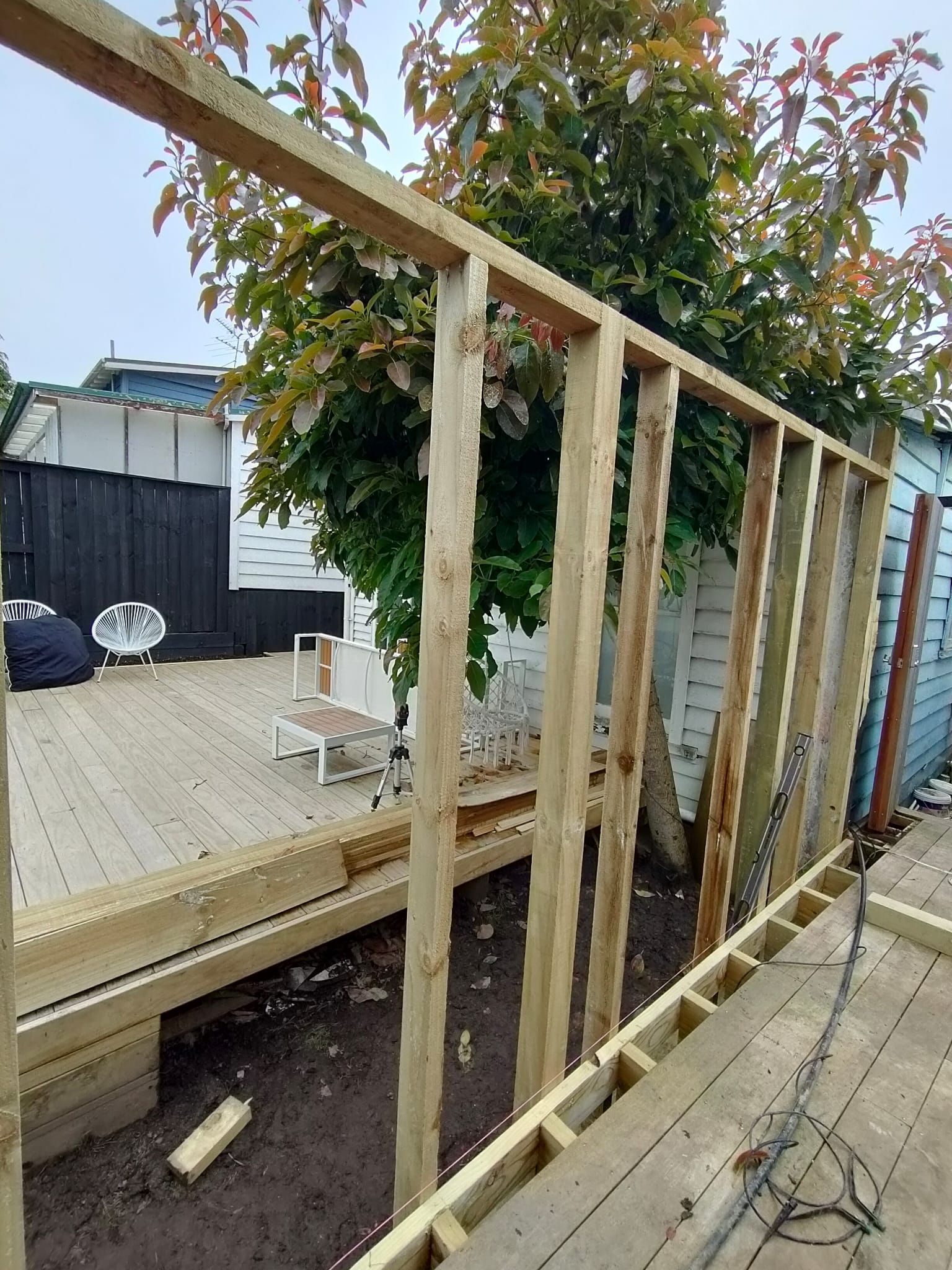 Wooden frame structure being built outdoors. Framing on decking with backyard in background.