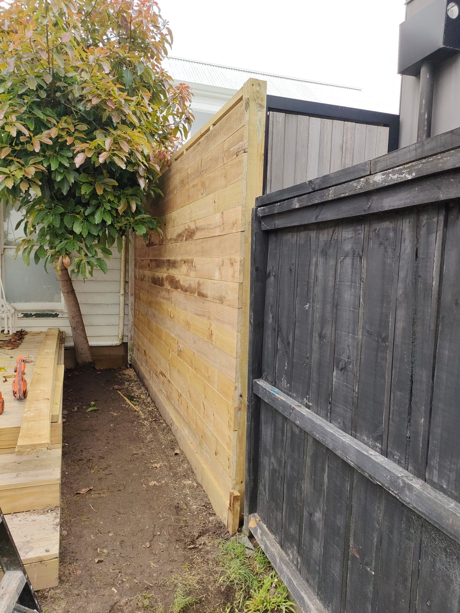 Wooden fence extending from a house, next to a black fence and a tree.