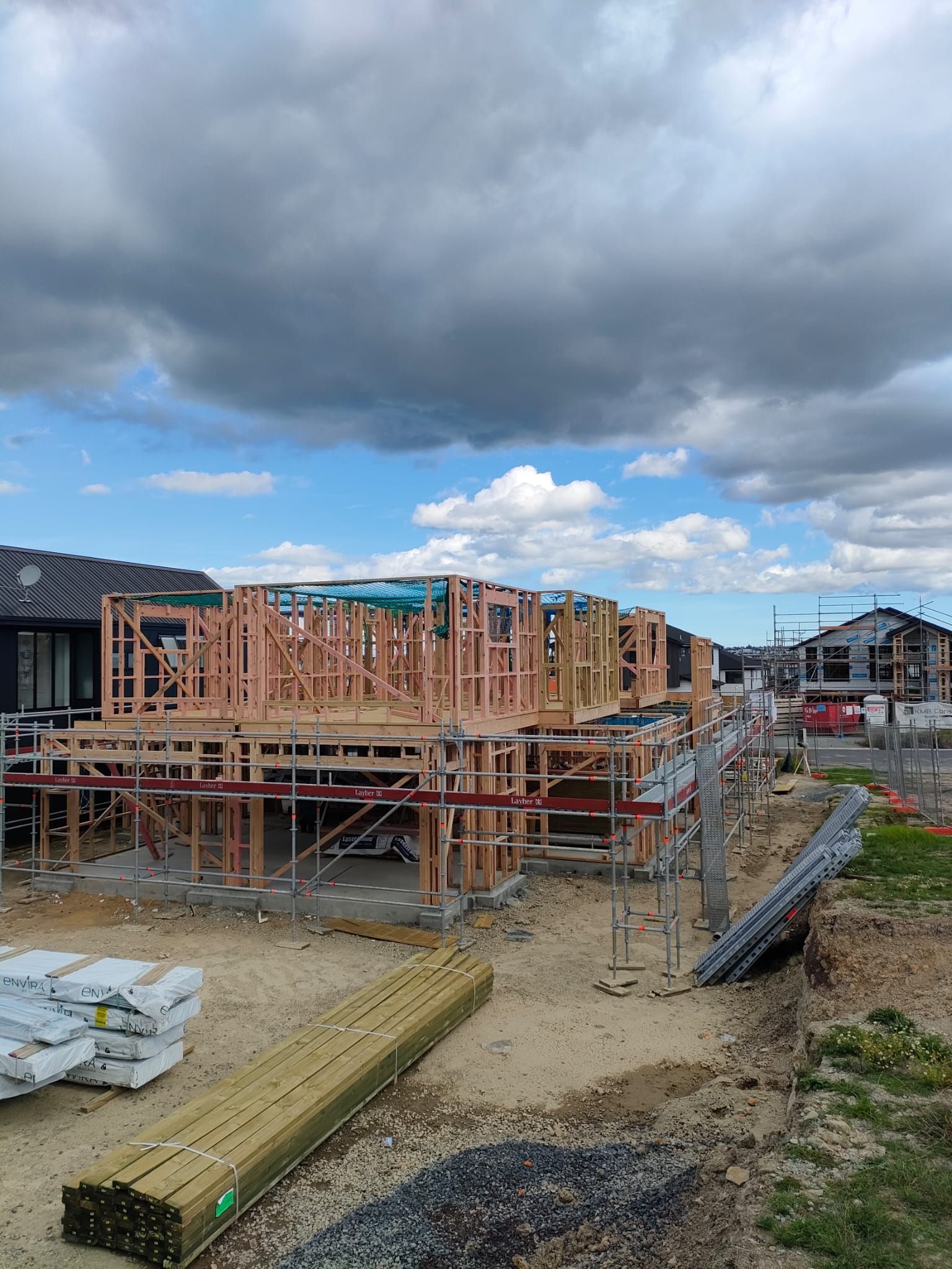 Construction site with wooden framing under cloudy sky; other houses are in the background.