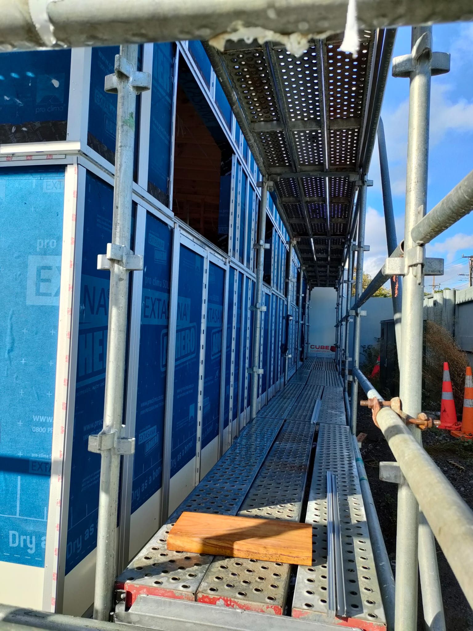 Scaffolding next to a building under construction. Blue weather-resistant barrier visible.