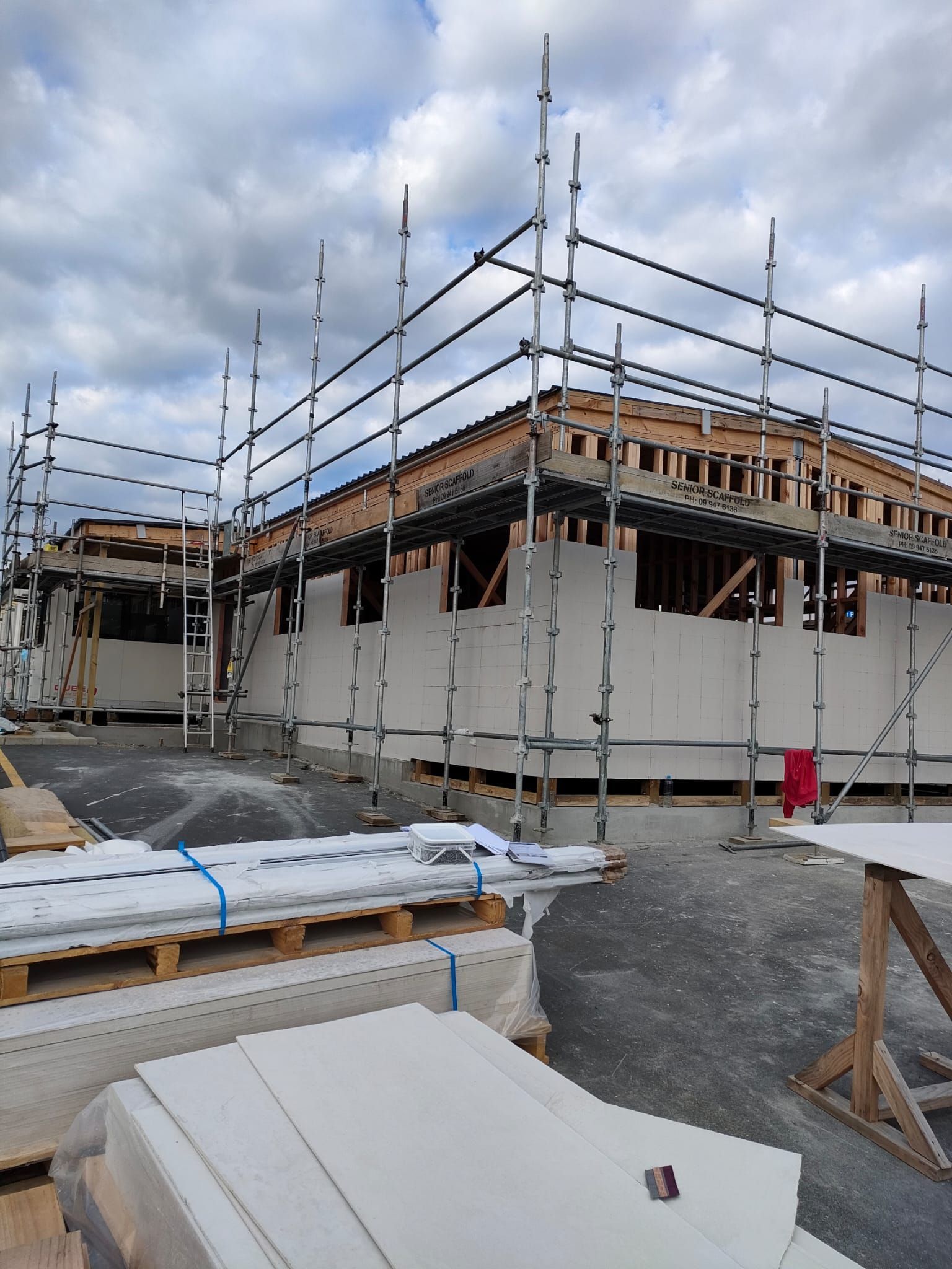 Construction site with scaffolding around a partially built building with light-colored walls and exposed wooden framing.