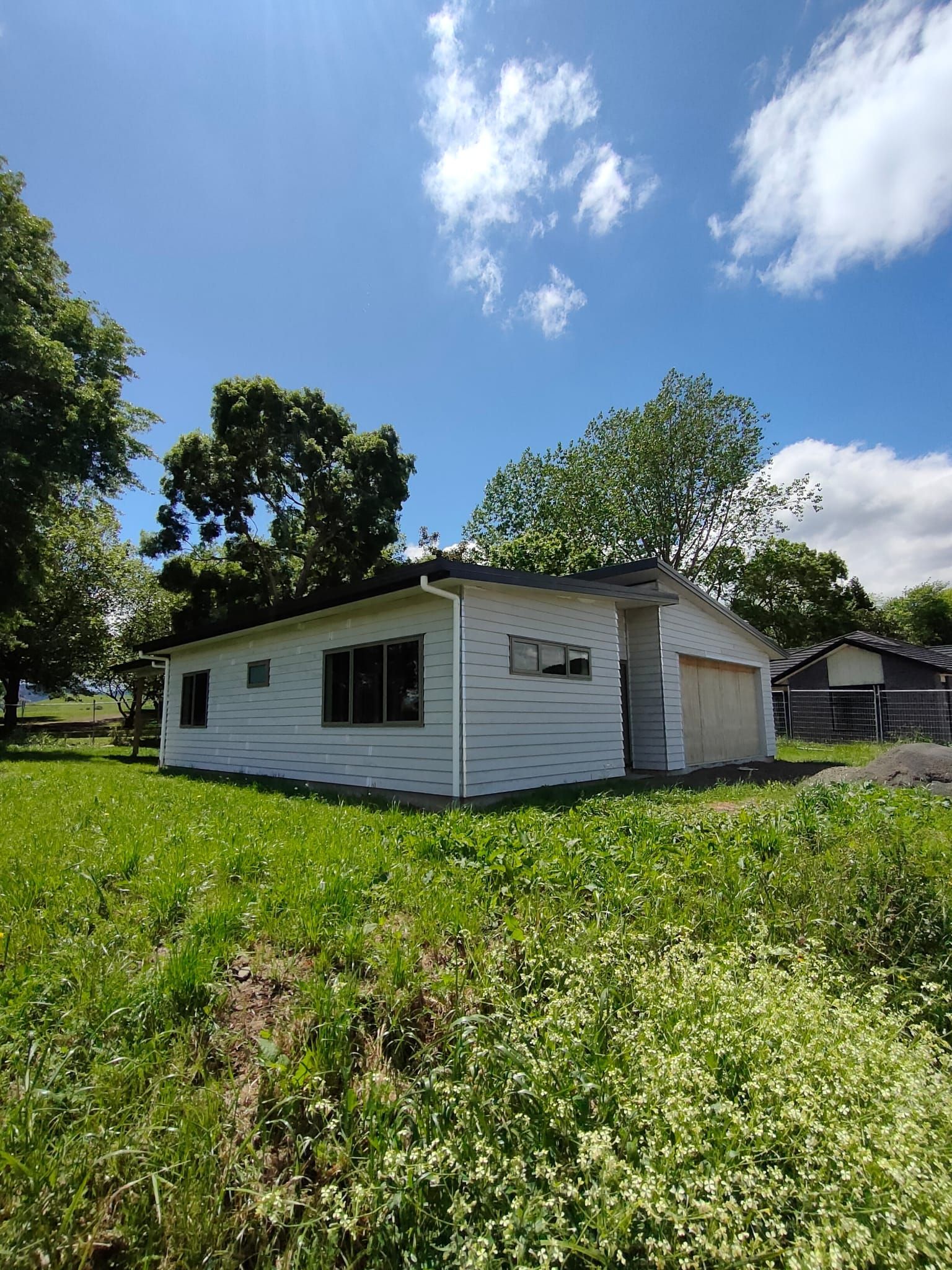 White house with a garage, surrounded by green grass and trees, under a blue sky with clouds.