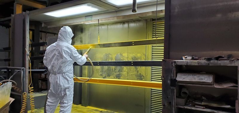 A Man in a Protective Suit is Spraying Yellow Paint on a Piece of Metal