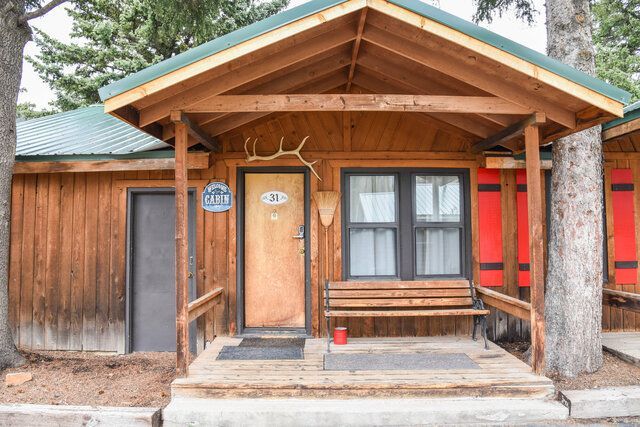 Cabin exterior with porch, door, bench, and antlers. Brown wood, green roof. Number 28.