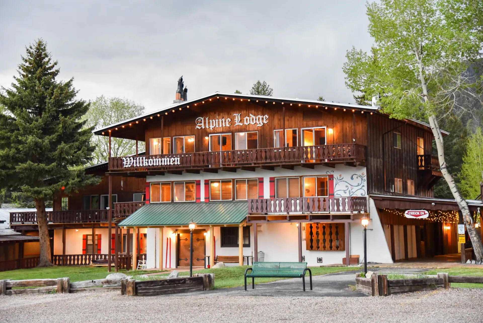 Alpine Lodge, a multi-story wooden building with a green awning, and a bench outside.