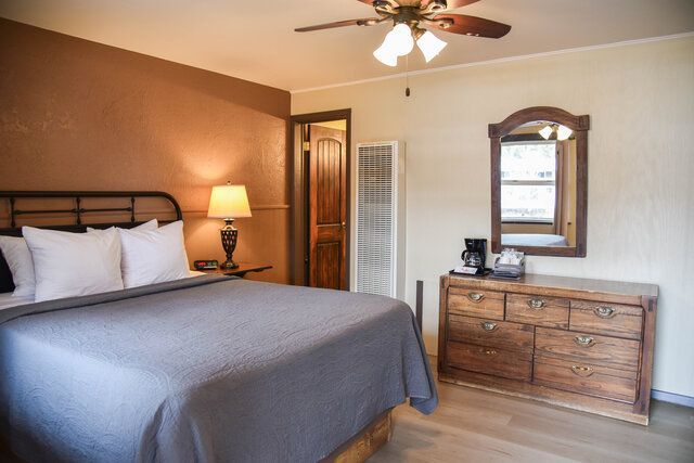 Bedroom with a bed, dresser, mirror, and lamp, brown and beige tones, soft lighting.