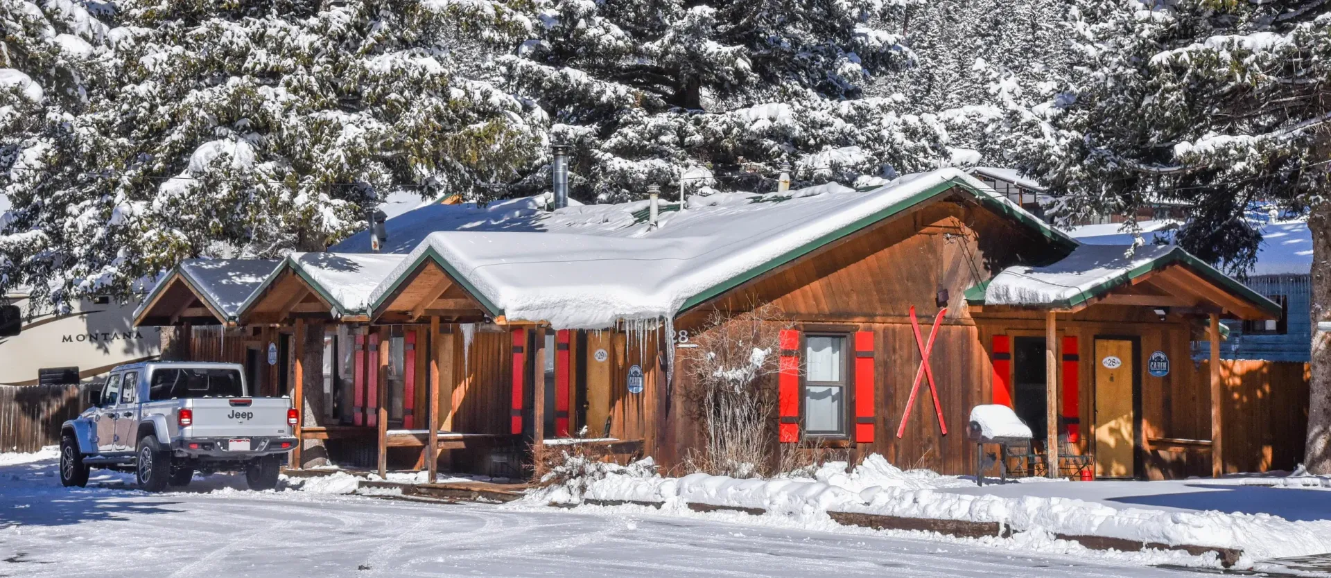 A snowy, brown wooden building with red shutters and a white pickup truck in front.