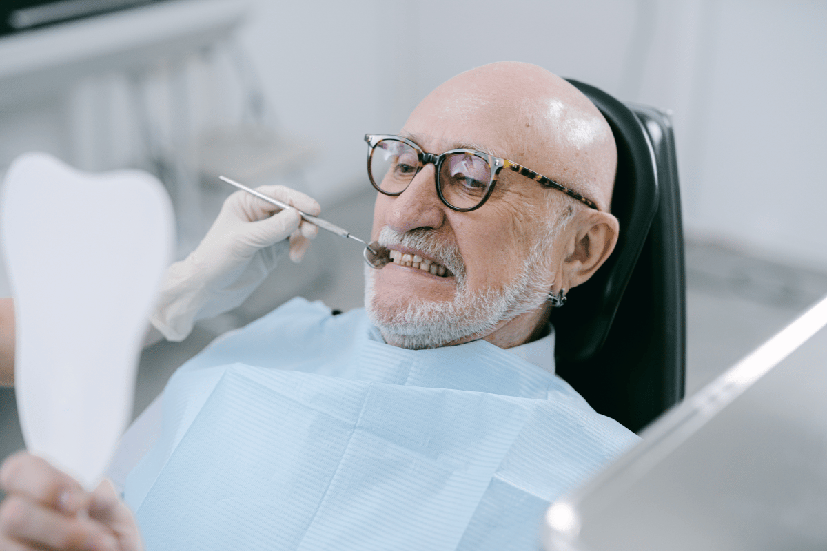 Man in glasses at dentist, mouth open, being examined with tools.