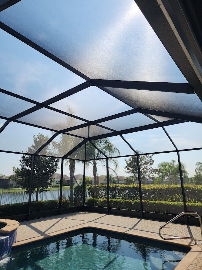 A swimming pool is surrounded by a screened in area with chairs and umbrellas.