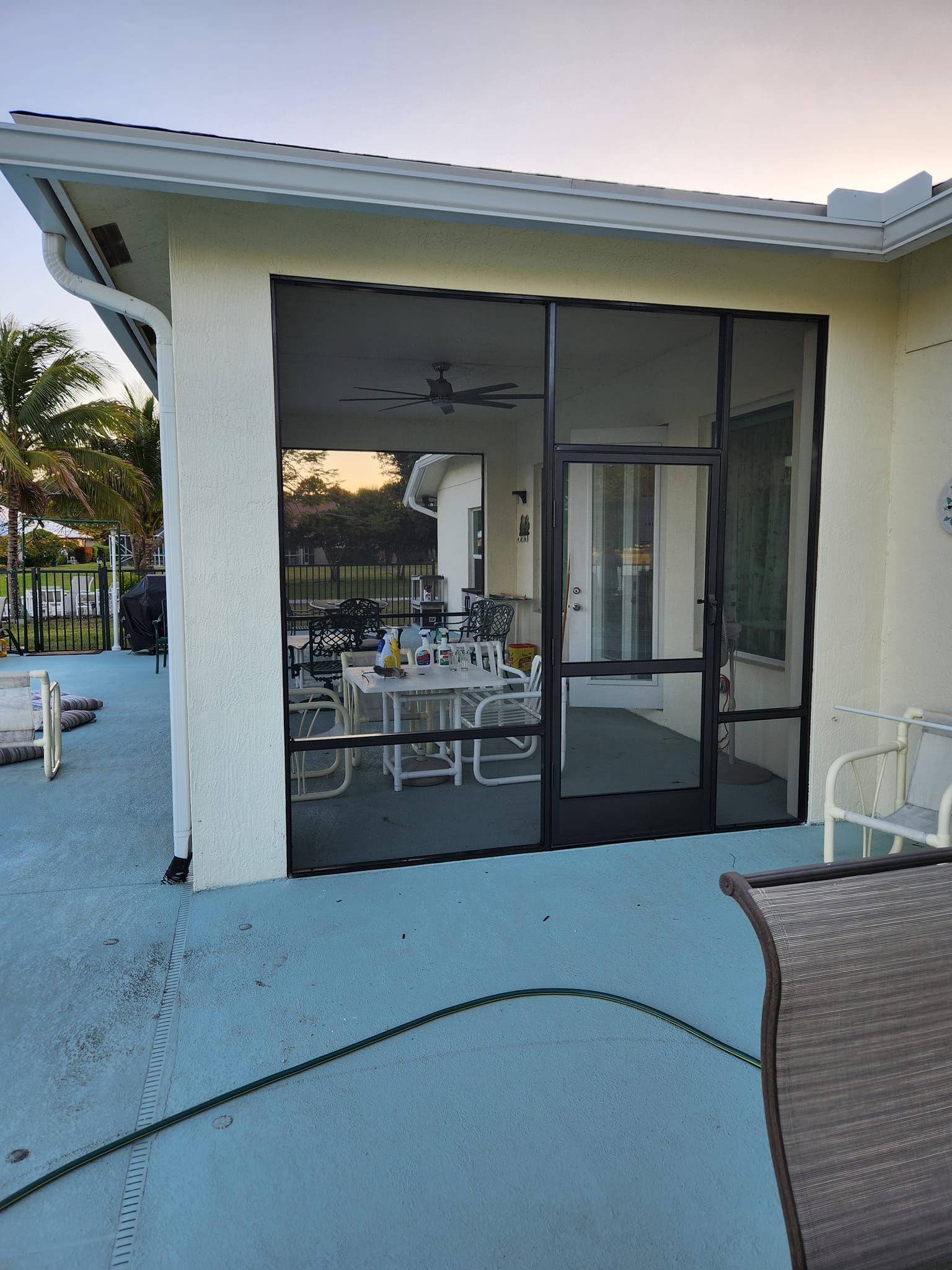 A screened in porch with tables and chairs and a hose.